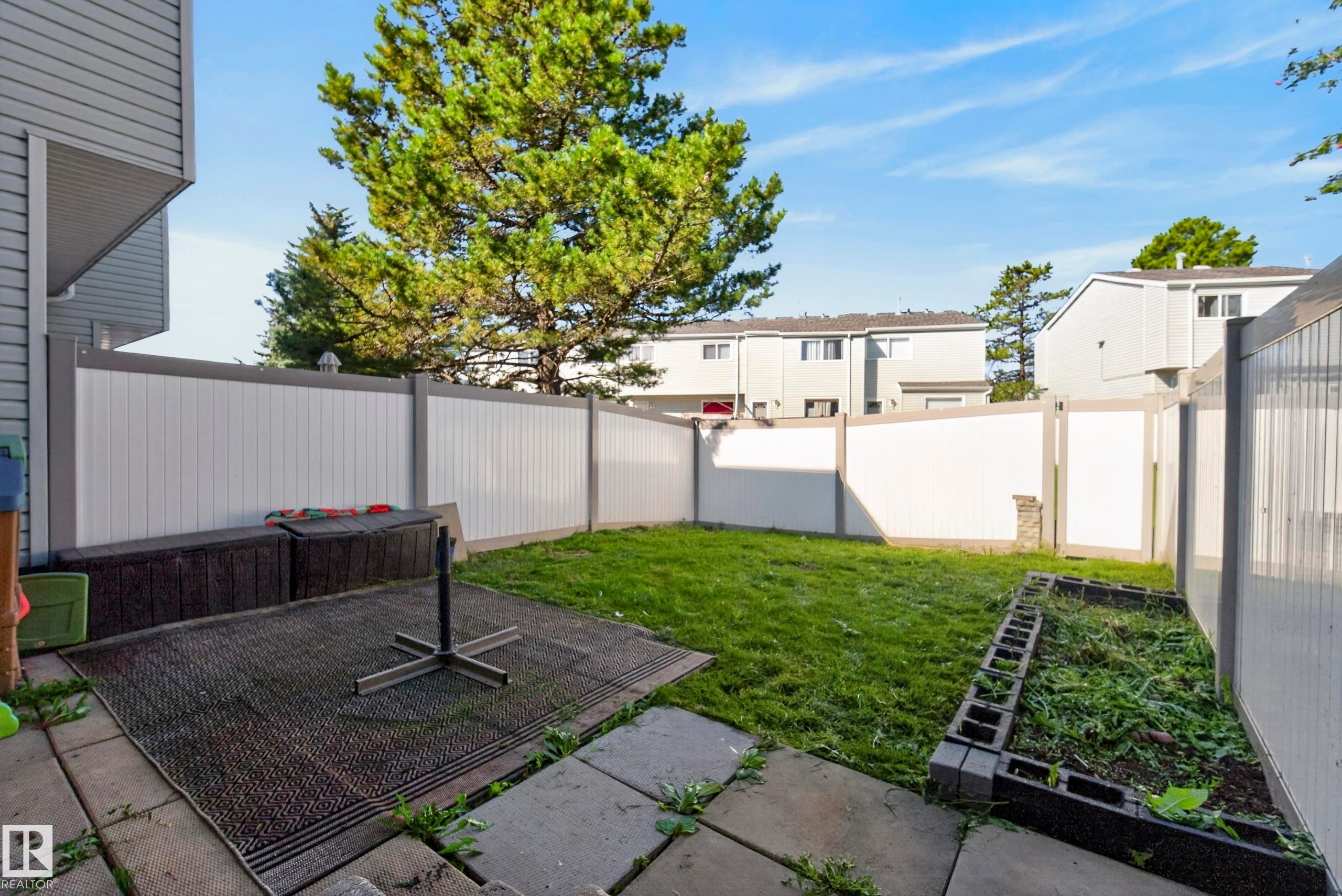 Private fenced backyard featuring a grassy area, concrete patio, and garden bed - 141 Dickinsfield Court Nw, Edmonton, AB