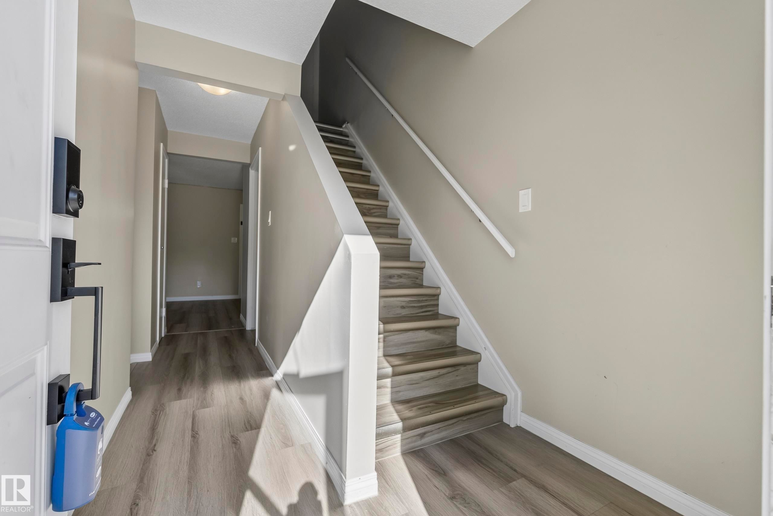 Staircase with wood-finish treads and risers, complemented by coordinating wood-finish flooring in the hallway - 141 Dickinsfield Court Nw, Edmonton, AB