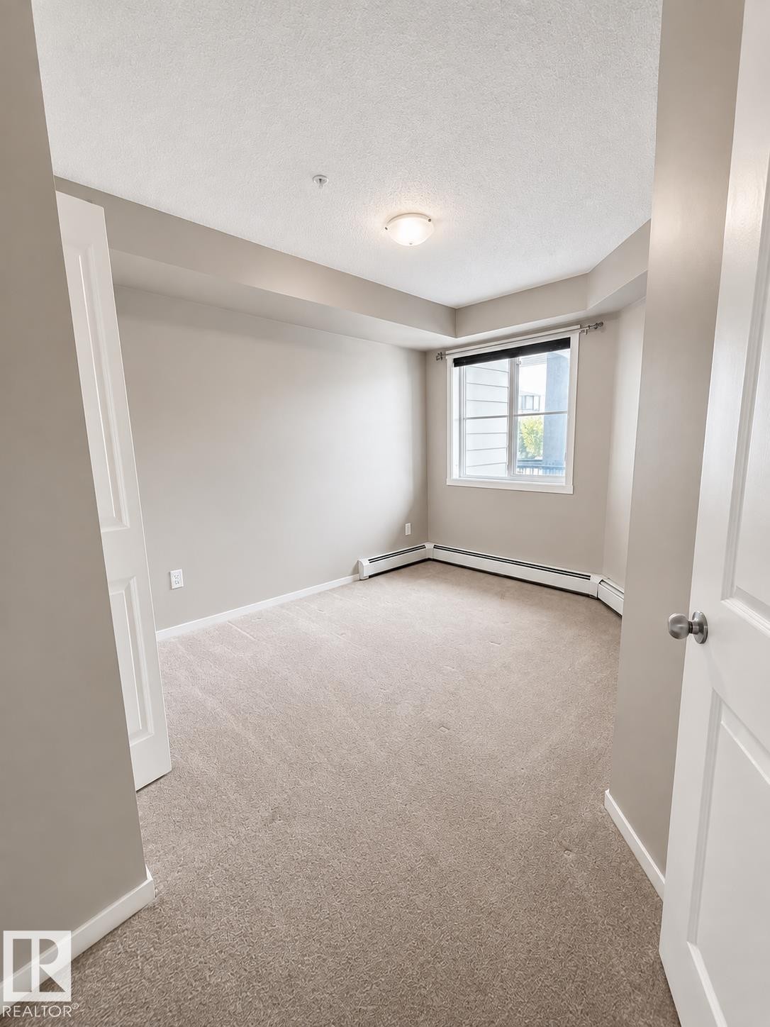 Neutral-toned carpeting, white trim, and a window with blinds - #208 18122 77 St Nw, Edmonton, AB