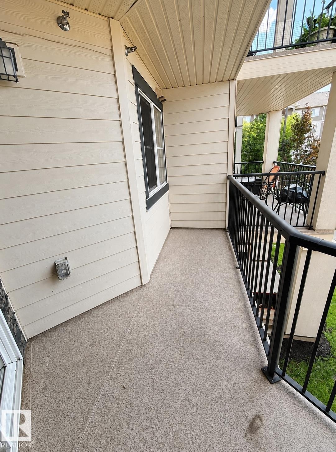 Balcony with black metal railings, textured light-colored flooring, and light-toned siding - #208 18122 77 St Nw, Edmonton, AB