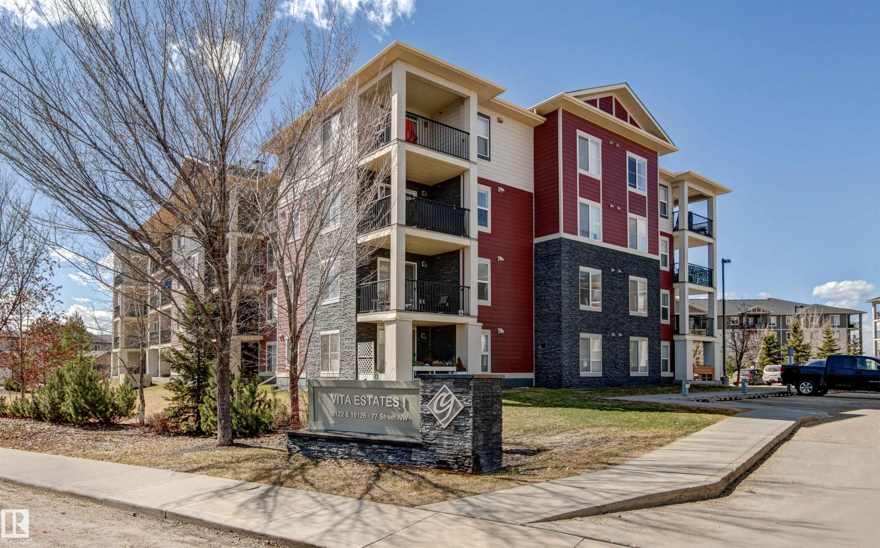 Modern multi-story building featuring red siding and dark stone veneer - #208 18122 77 St Nw, Edmonton, AB
