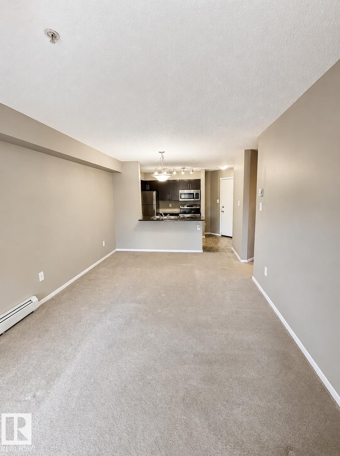 Open concept living area with carpeting, a kitchen featuring dark wood-finish cabinetry, stainless steel appliances, and a breakfast bar - #208 18122 77 St Nw, Edmonton, AB