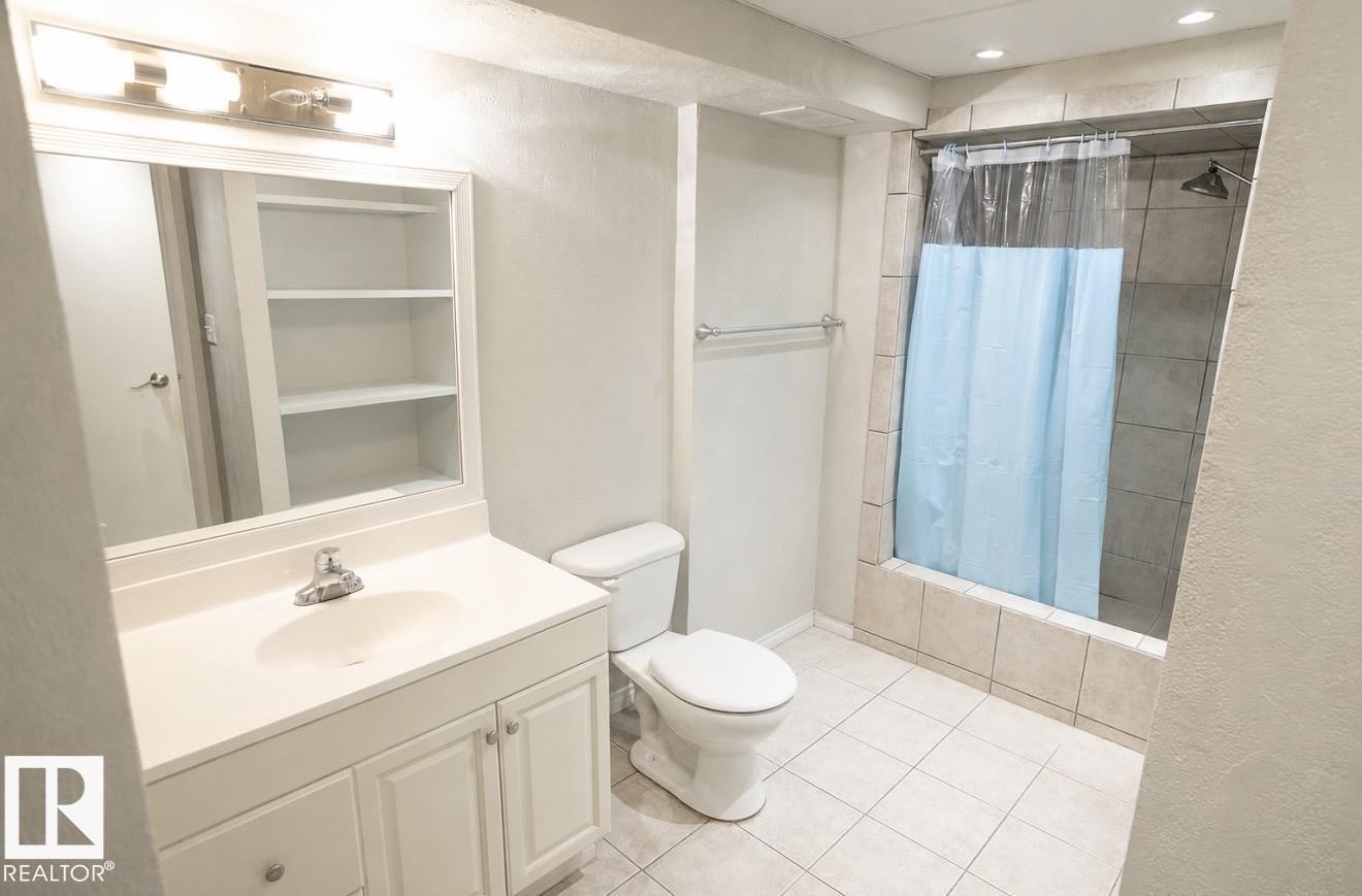 Vanity with integrated sink, mirrored medicine cabinet with shelving, tiled shower with tub, and ceramic tile flooring - 10439 36A Ave Nw, Edmonton, AB