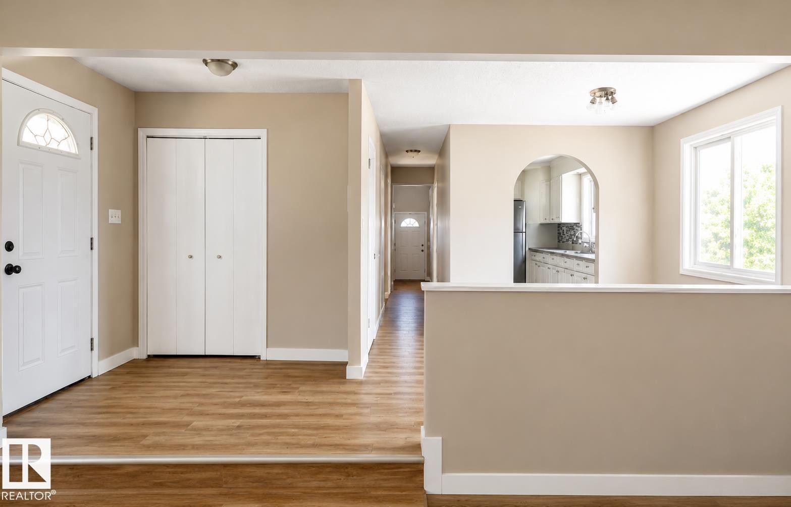 Wood-finish flooring throughout, entry door with decorative glass, bi-fold closet doors, arched doorway, and a double-pane window - 10439 36A Ave Nw, Edmonton, AB