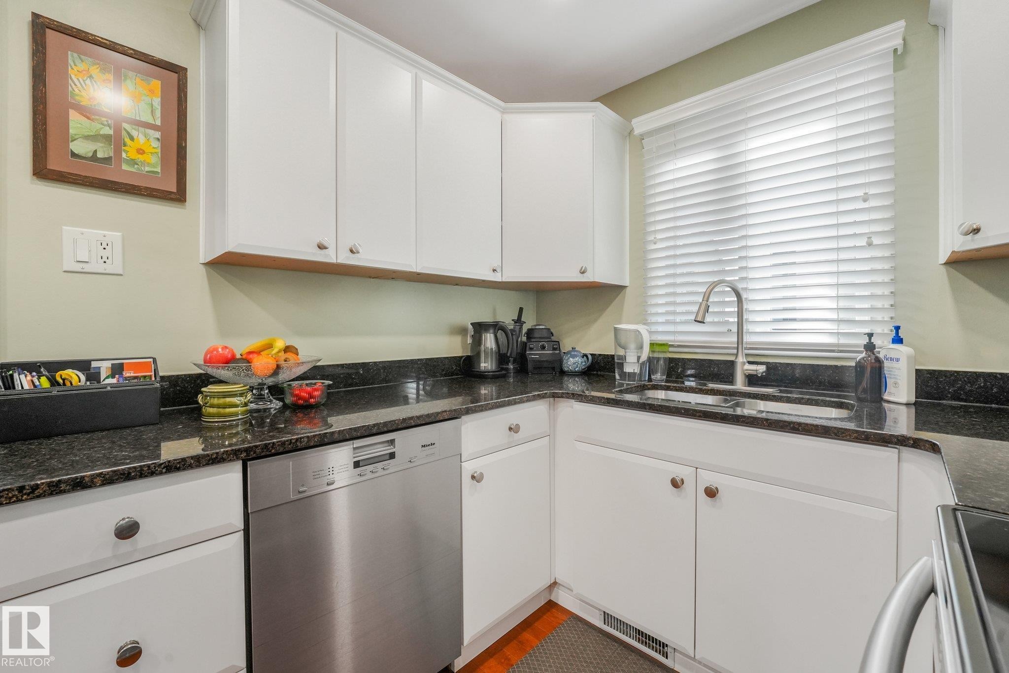 White cabinetry with silver-tone hardware, granite countertops, stainless steel dishwasher, and a stainless steel gooseneck faucet - 10531 137 Street Nw, Edmonton, AB