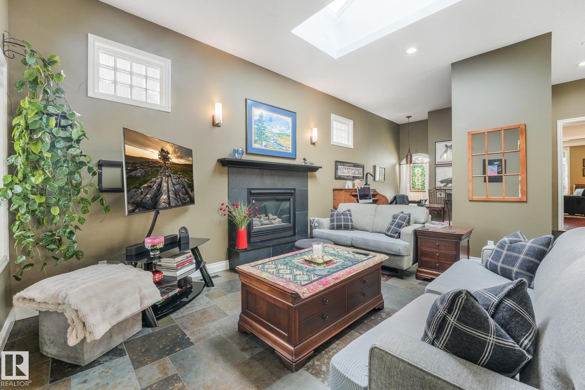 Recessed lighting, skylight, slate tile flooring, wall sconces, and a gas fireplace with a dark tile surround - 10531 137 Street Nw, Edmonton, AB