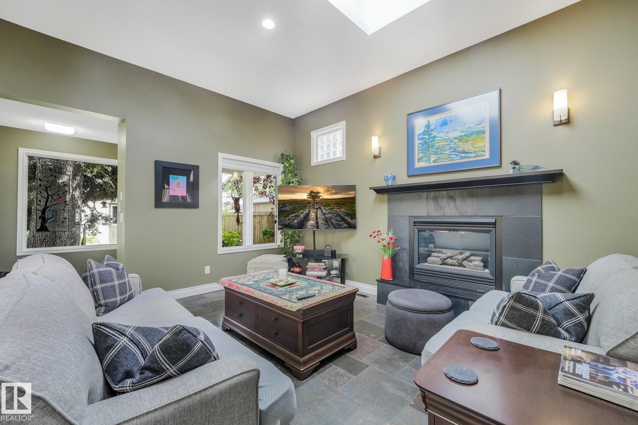 Living area featuring a fireplace with a stone surround, a skylight, recessed lighting, and wall sconces - 10531 137 Street Nw, Edmonton, AB