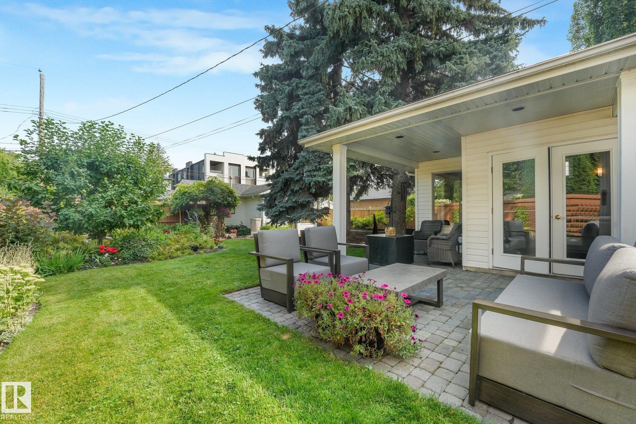 Expansive backyard featuring a covered patio, paved stone hardscaping, lush green lawn, and mature landscaping - 10531 137 Street Nw, Edmonton, AB
