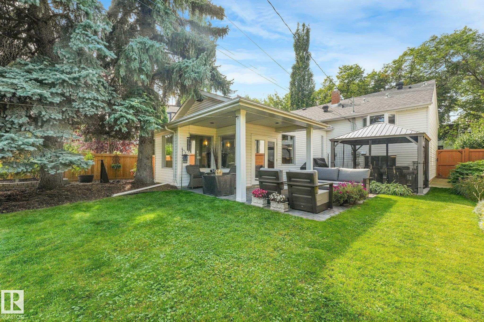 Spacious backyard retreat featuring a manicured lawn, mature evergreen and deciduous trees, and a modern covered patio with white columns - 10531 137 Street Nw, Edmonton, AB