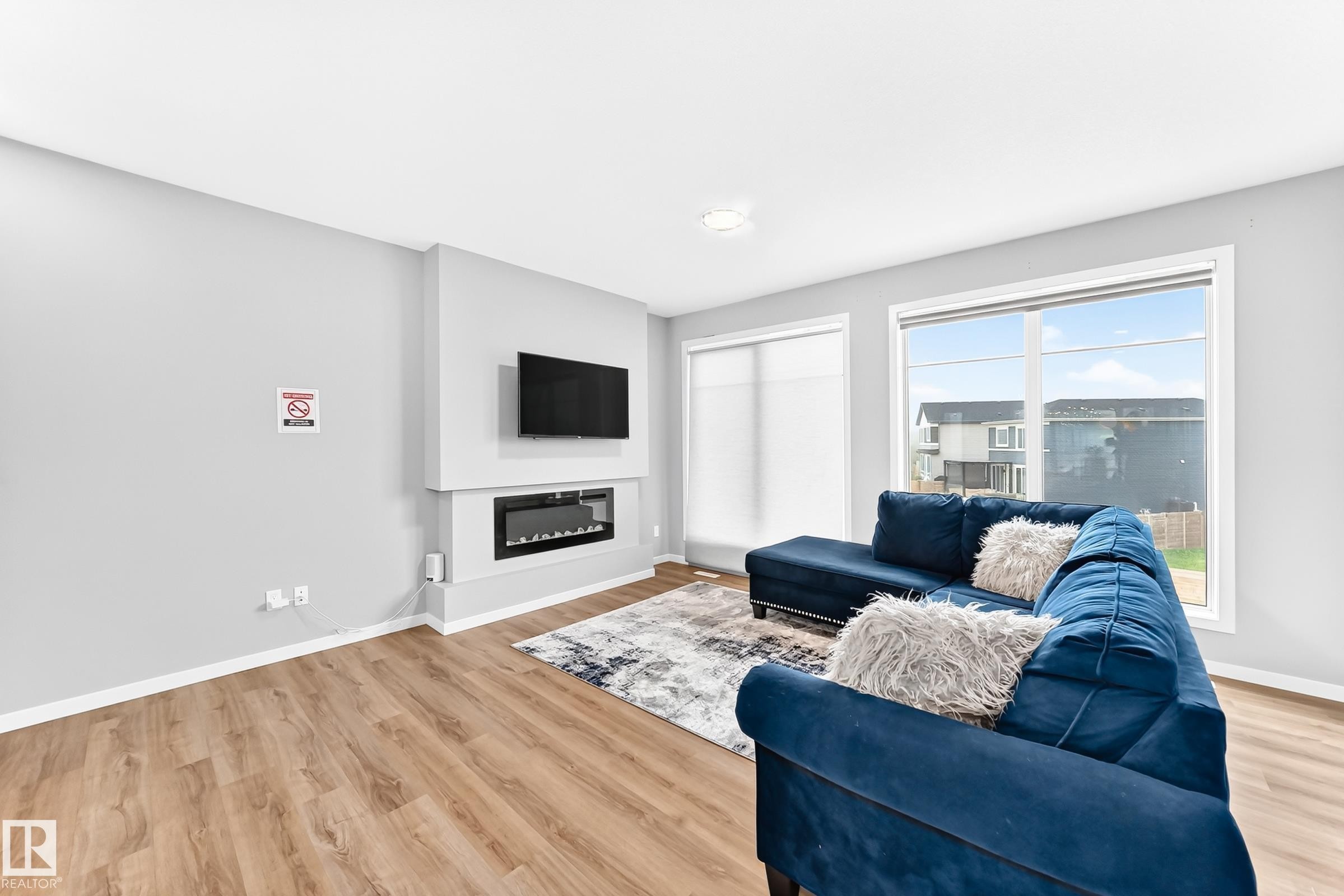 Living space featuring wood-finish flooring, a built-in electric fireplace, and large windows with roller shades - 479 39 St Sw, Edmonton, AB