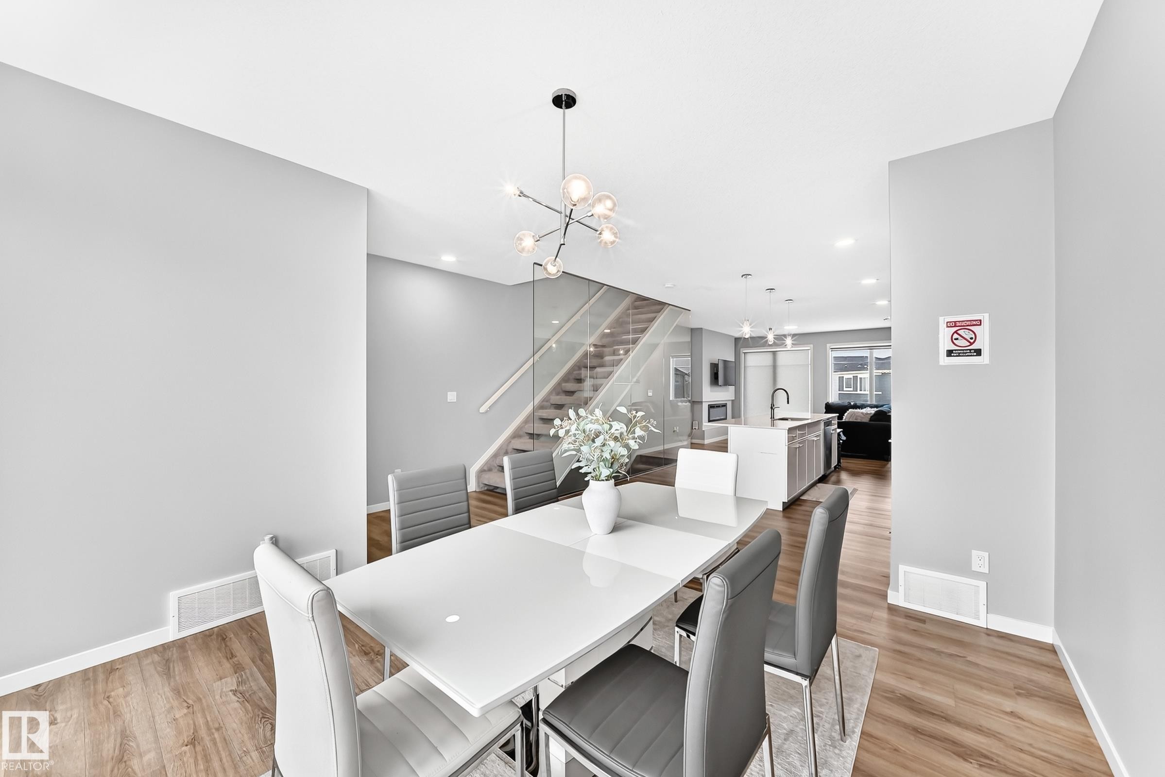 Open-concept dining area with wood-finish flooring, a contemporary chandelier, and a glass-paneled staircase - 479 39 St Sw, Edmonton, AB