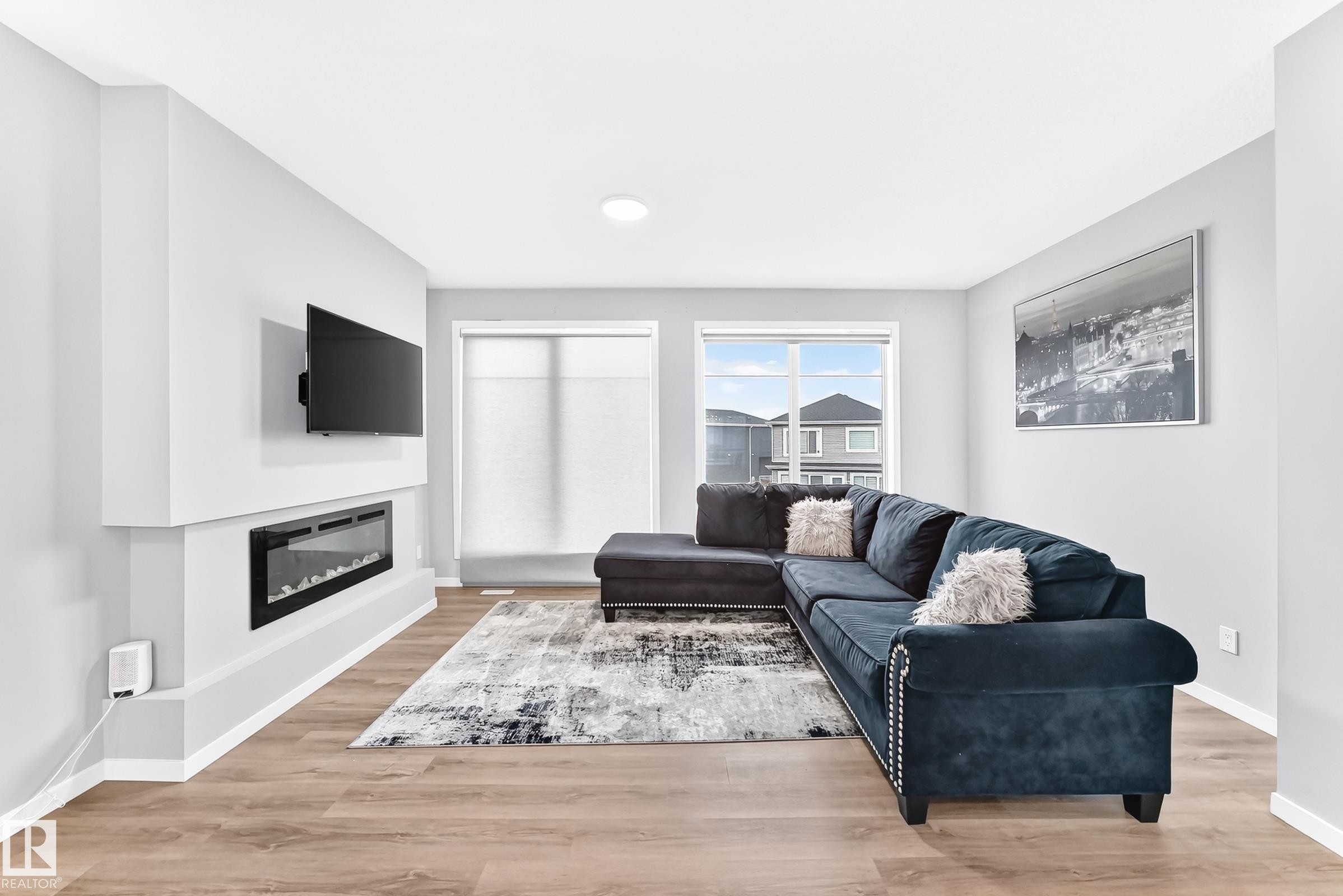 Spacious living area featuring wood-finish flooring, an electric fireplace, a recessed ceiling light, and white trim - 479 39 St Sw, Edmonton, AB