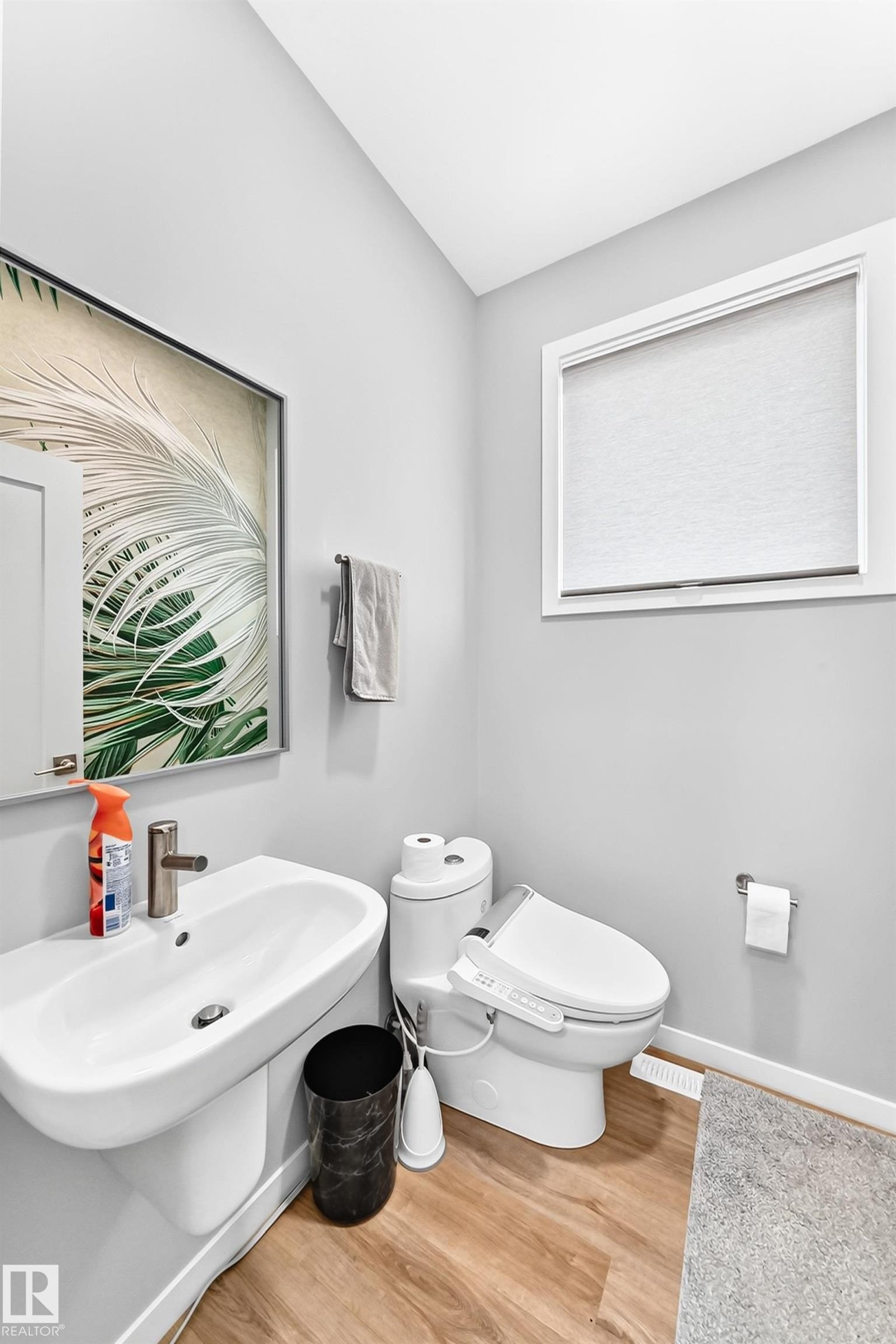 Pedestal sink with a single-hole faucet, modern toilet, and wood-finish flooring - 479 39 St Sw, Edmonton, AB