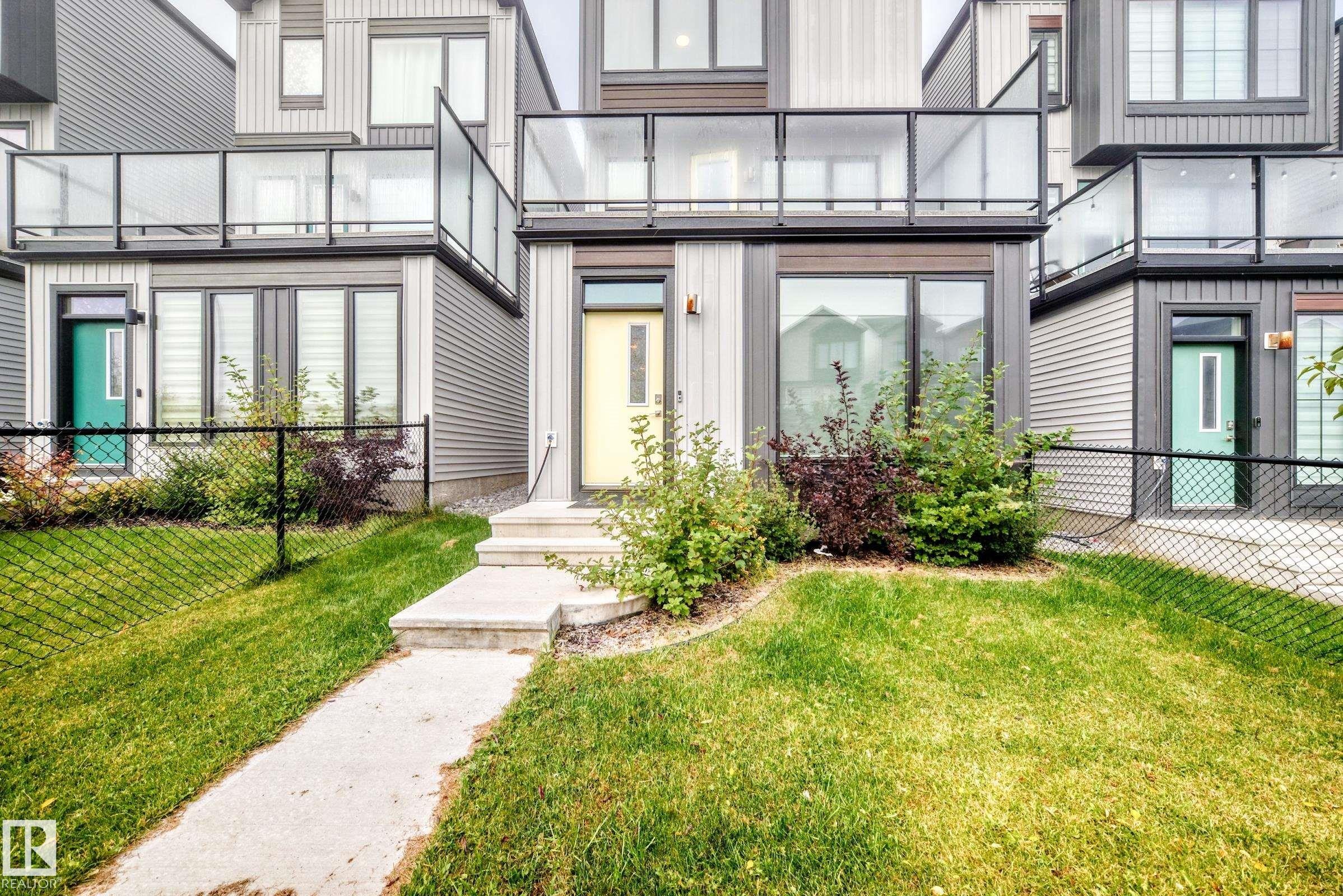 Modern multi-level exterior with a vibrant yellow front door and a concrete pathway - 479 39 St Sw, Edmonton, AB