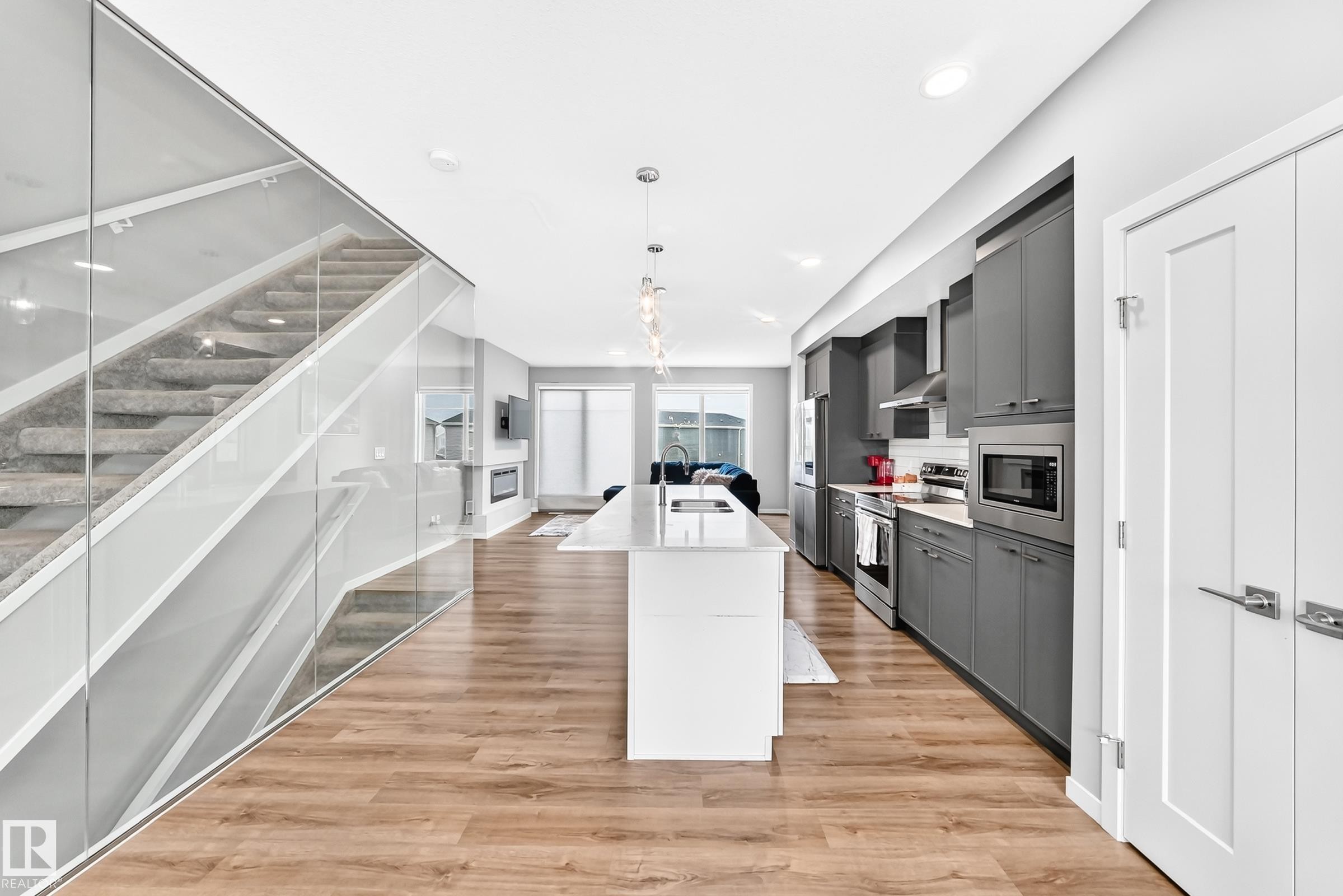 Wood-finish flooring throughout, kitchen featuring gray cabinetry, stainless steel appliances, and a central island with a waterfall countertop - 479 39 St Sw, Edmonton, AB