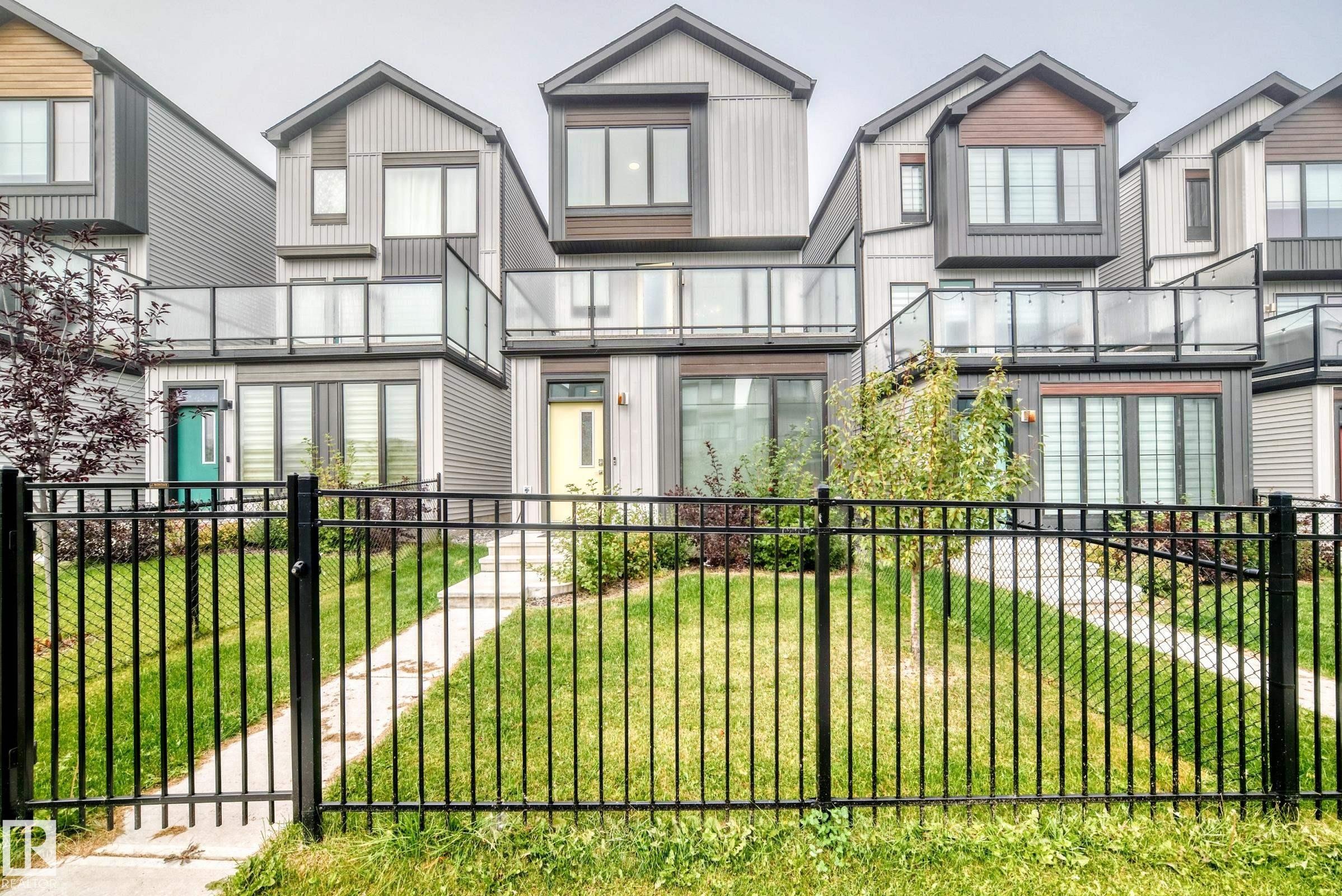 Modern exterior with multiple balconies featuring clear glass railings, a black metal fence, and a concrete pathway - 479 39 St Sw, Edmonton, AB
