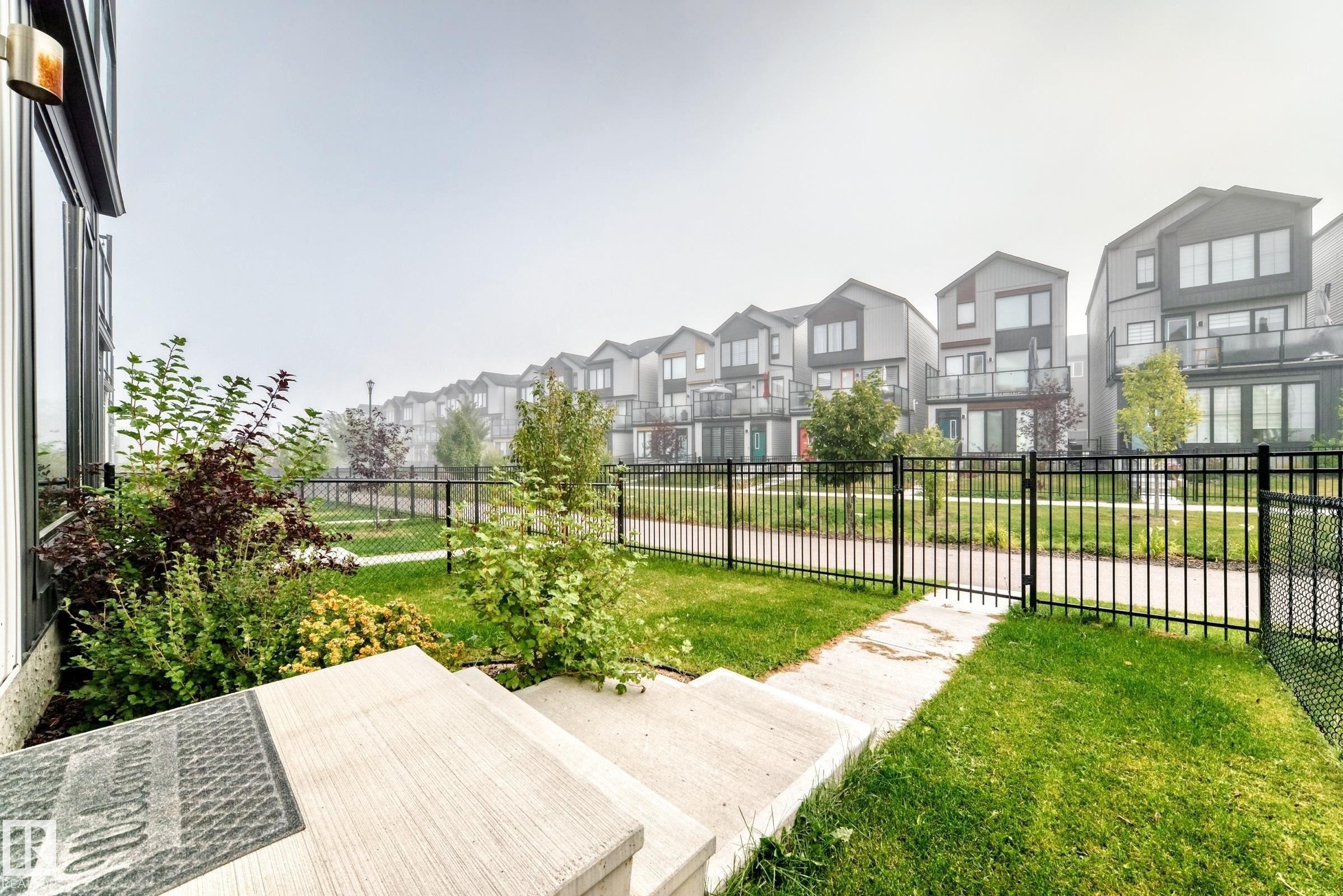 Concrete steps leading to a manicured lawn, established landscaping, and a black wrought iron fence - 479 39 St Sw, Edmonton, AB