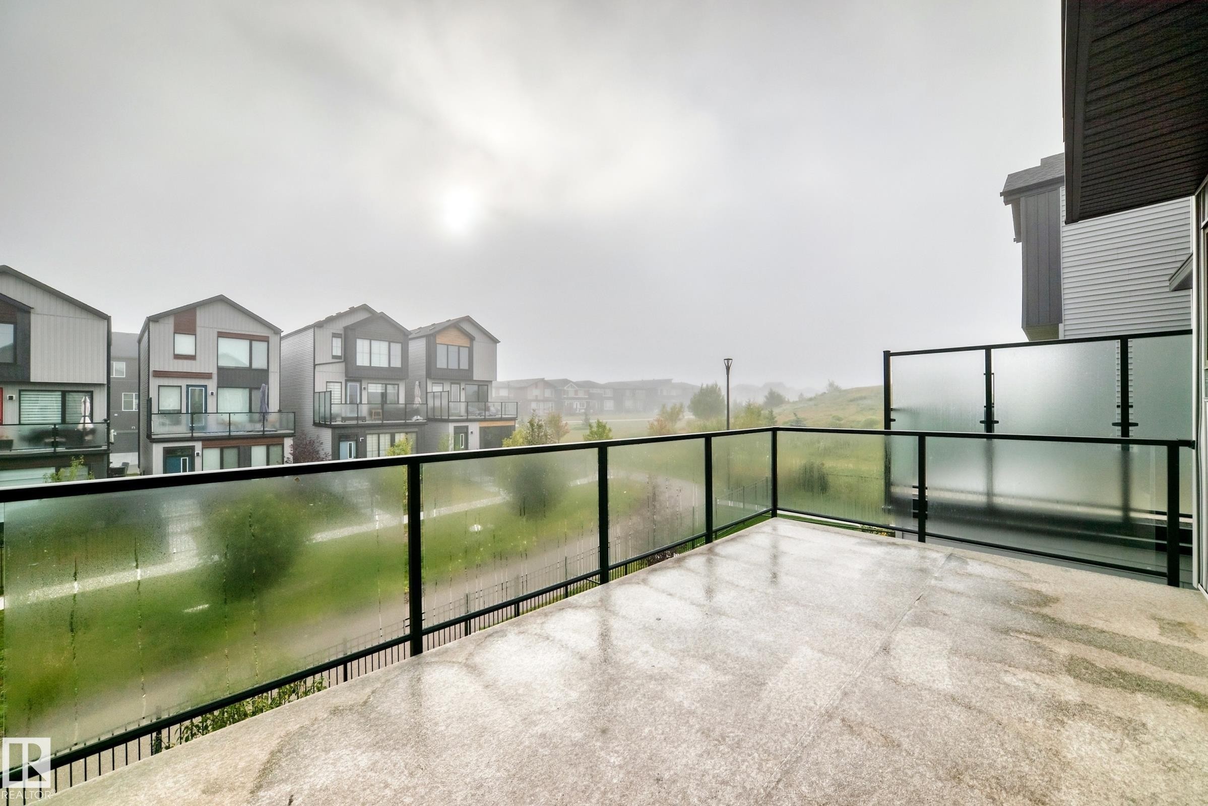 Spacious outdoor balcony with concrete flooring, clear glass railing, and frosted privacy glass panels - 479 39 St Sw, Edmonton, AB