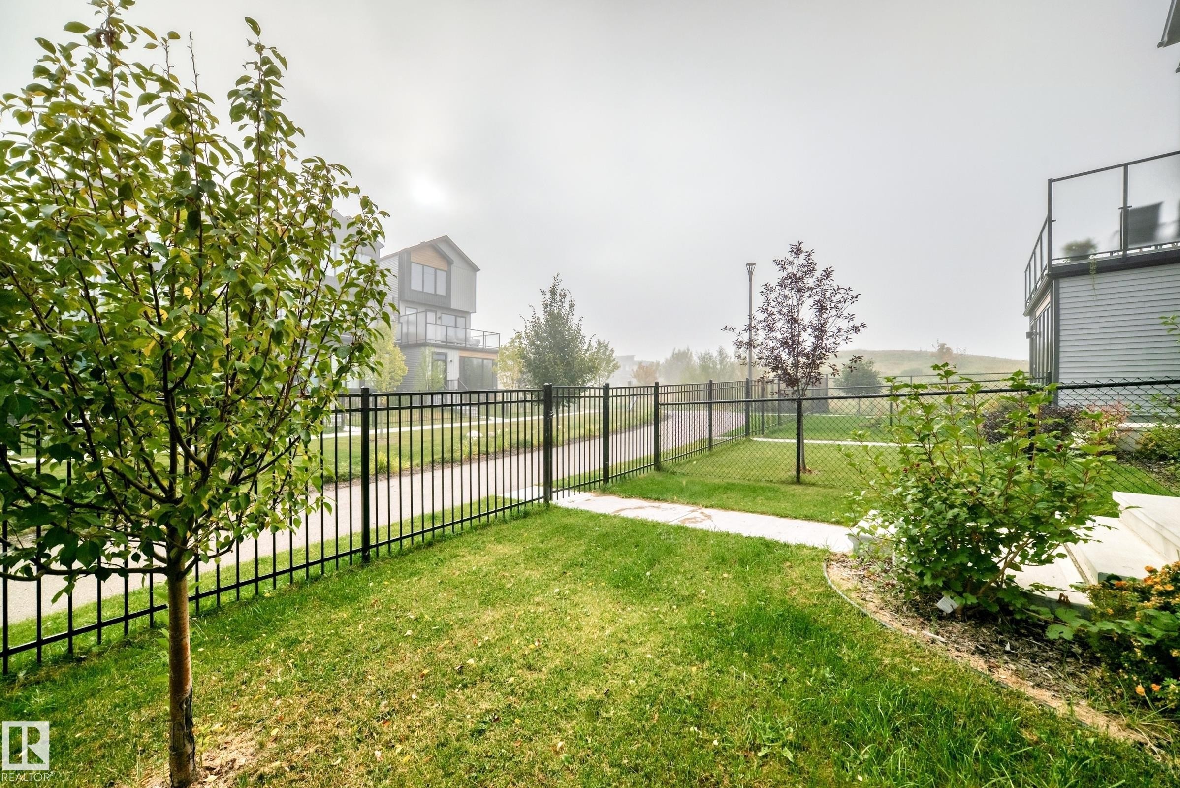 Landscaped yard with mature plantings, black metal fencing, and concrete pathway - 479 39 St Sw, Edmonton, AB