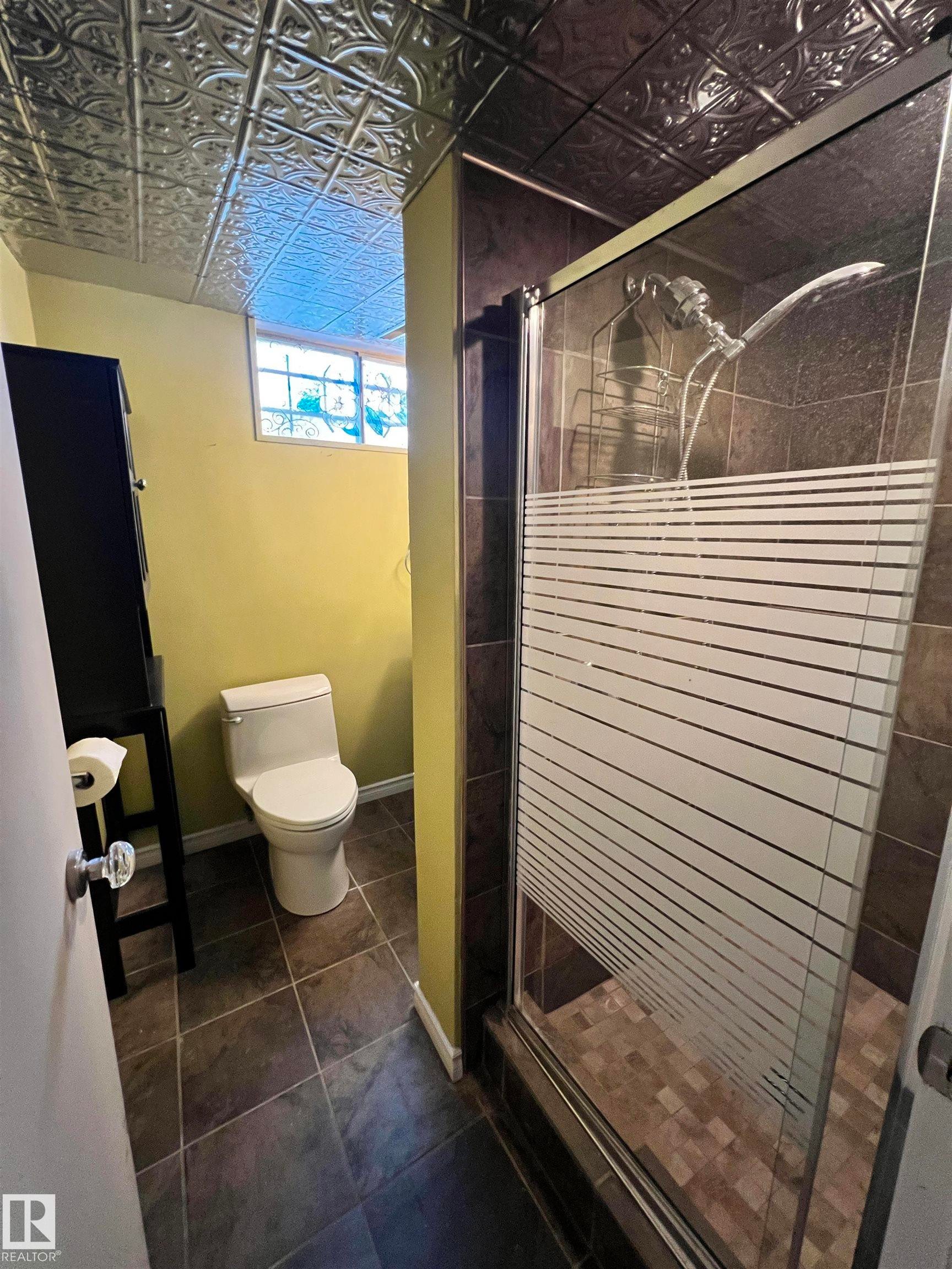 Textured ceiling paneling, glass-enclosed shower, dark tile flooring, block window, and a modern toilet - 15003 81 Street Nw, Edmonton, AB