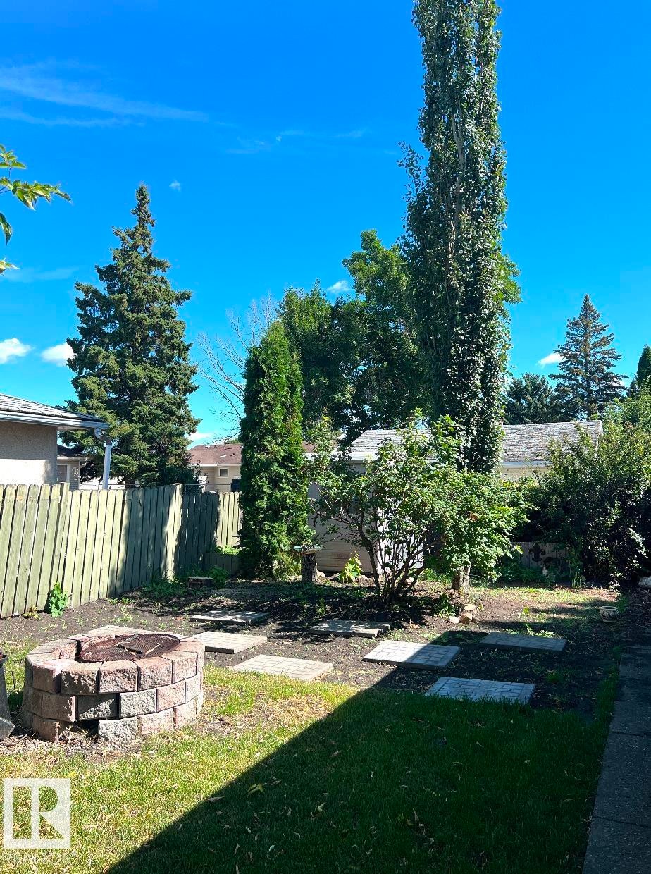 Expansive backyard featuring a stone-block fire pit, stepping stone pathway, and mature trees - 15003 81 Street Nw, Edmonton, AB