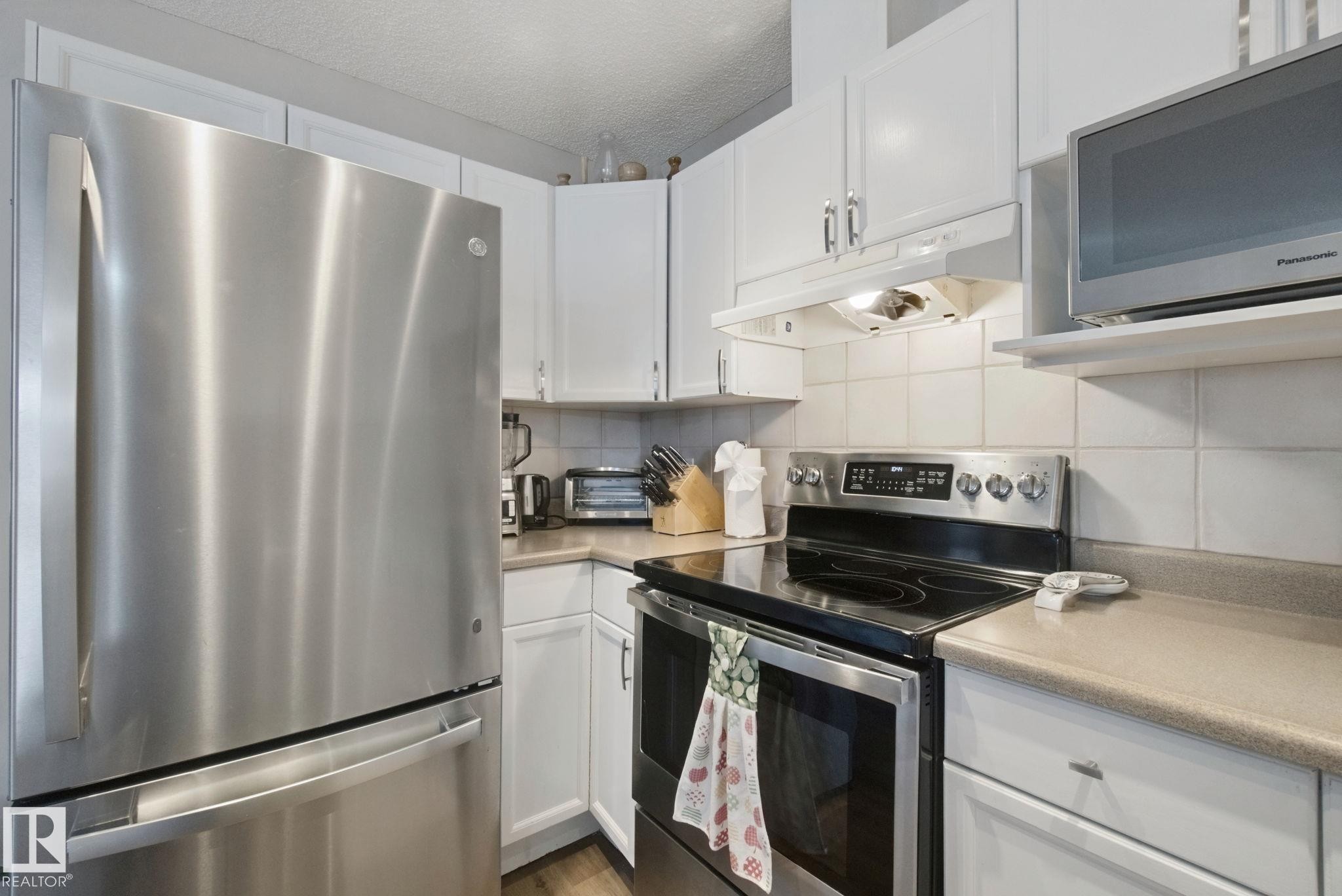 Stainless steel French door refrigerator, white upper and lower cabinetry, stainless steel range with ceramic cooktop, and a matching stainless steel over-the-range microwave - 15618 141 Street Nw, Edmonton, AB