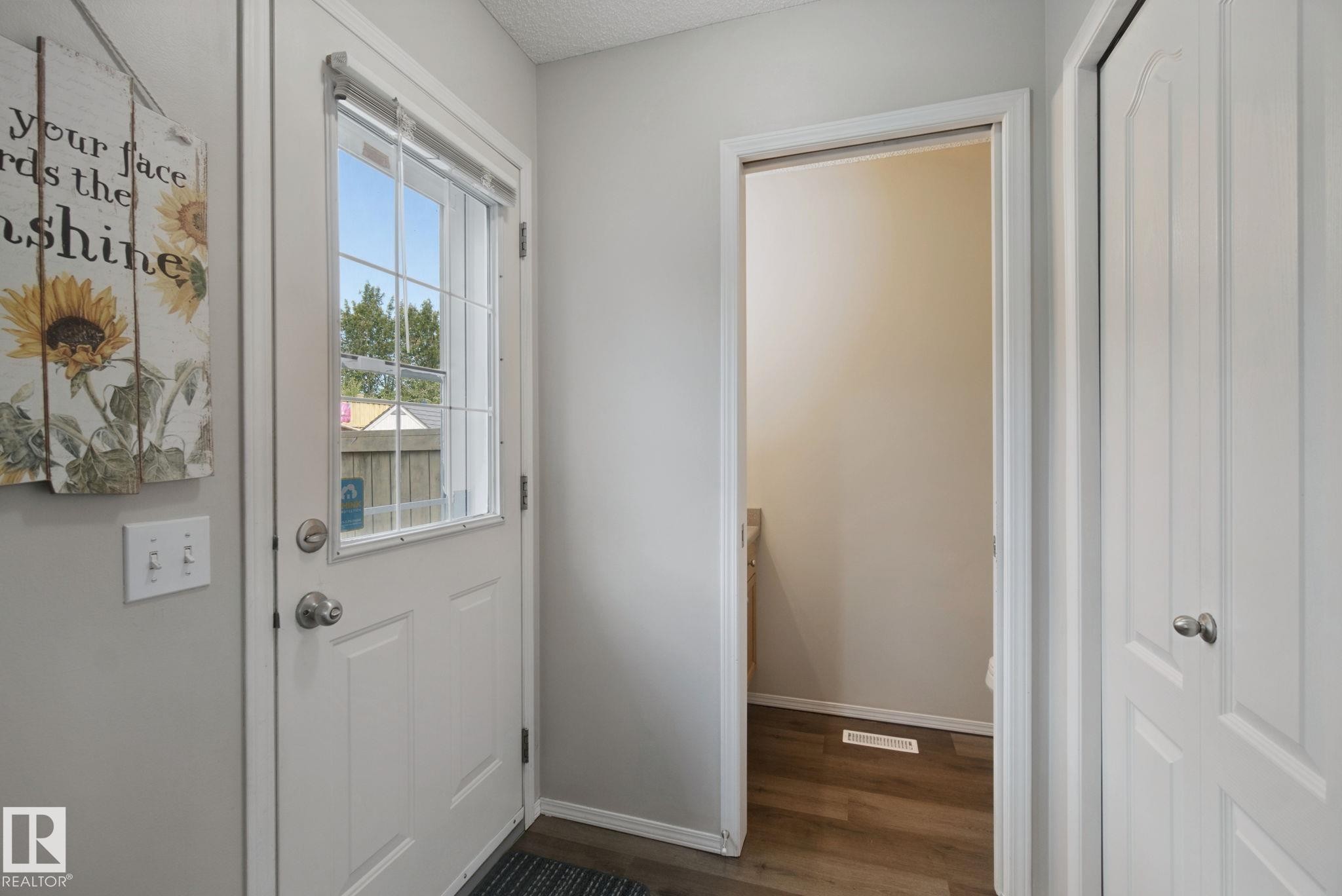 Entryway featuring a white paneled door with an integrated window, wood-finish flooring, and a white bi-fold closet door - 15618 141 Street Nw, Edmonton, AB
