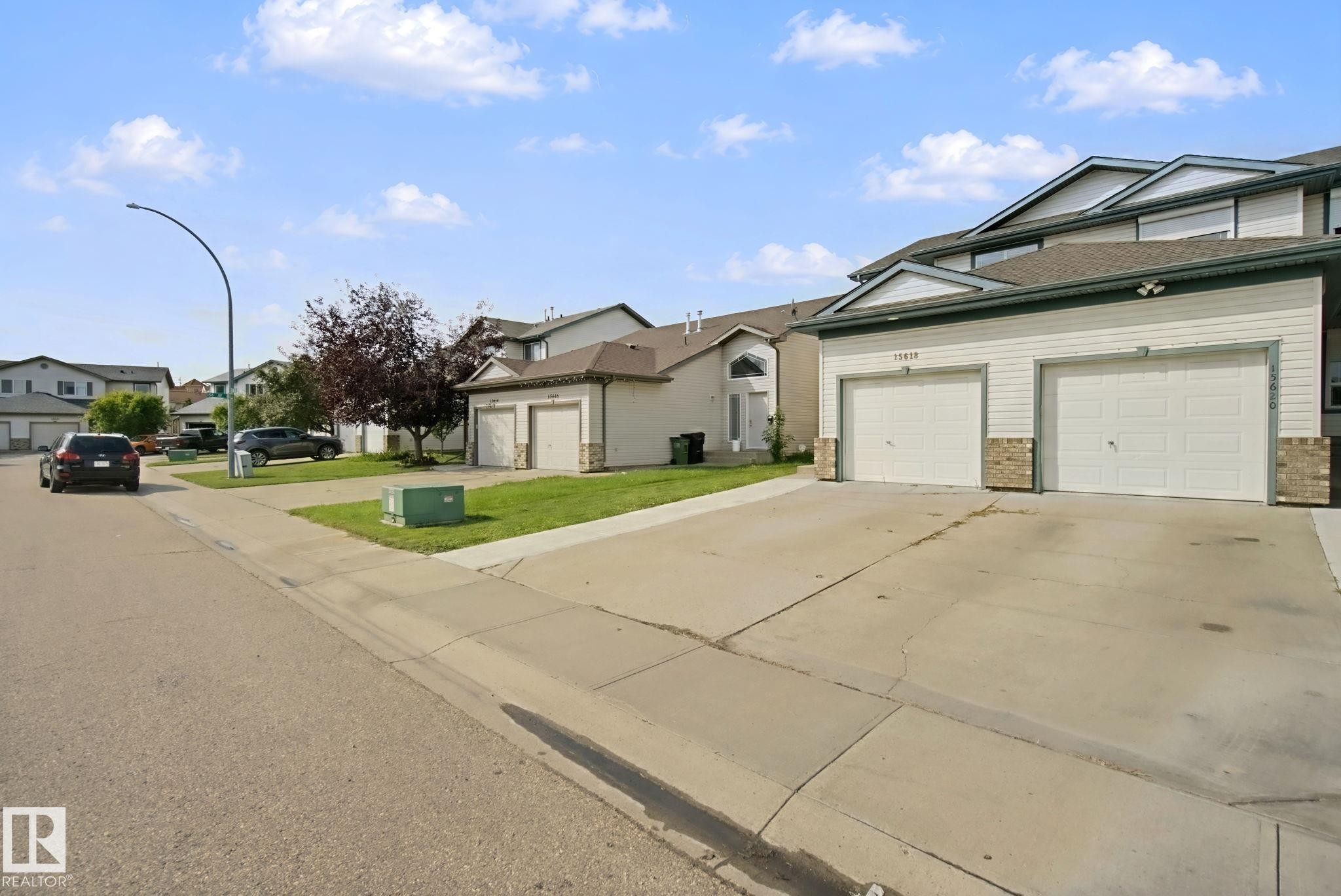 Exterior with light-colored siding and brick accents, featuring two attached garage doors and a paved driveway - 15618 141 Street Nw, Edmonton, AB