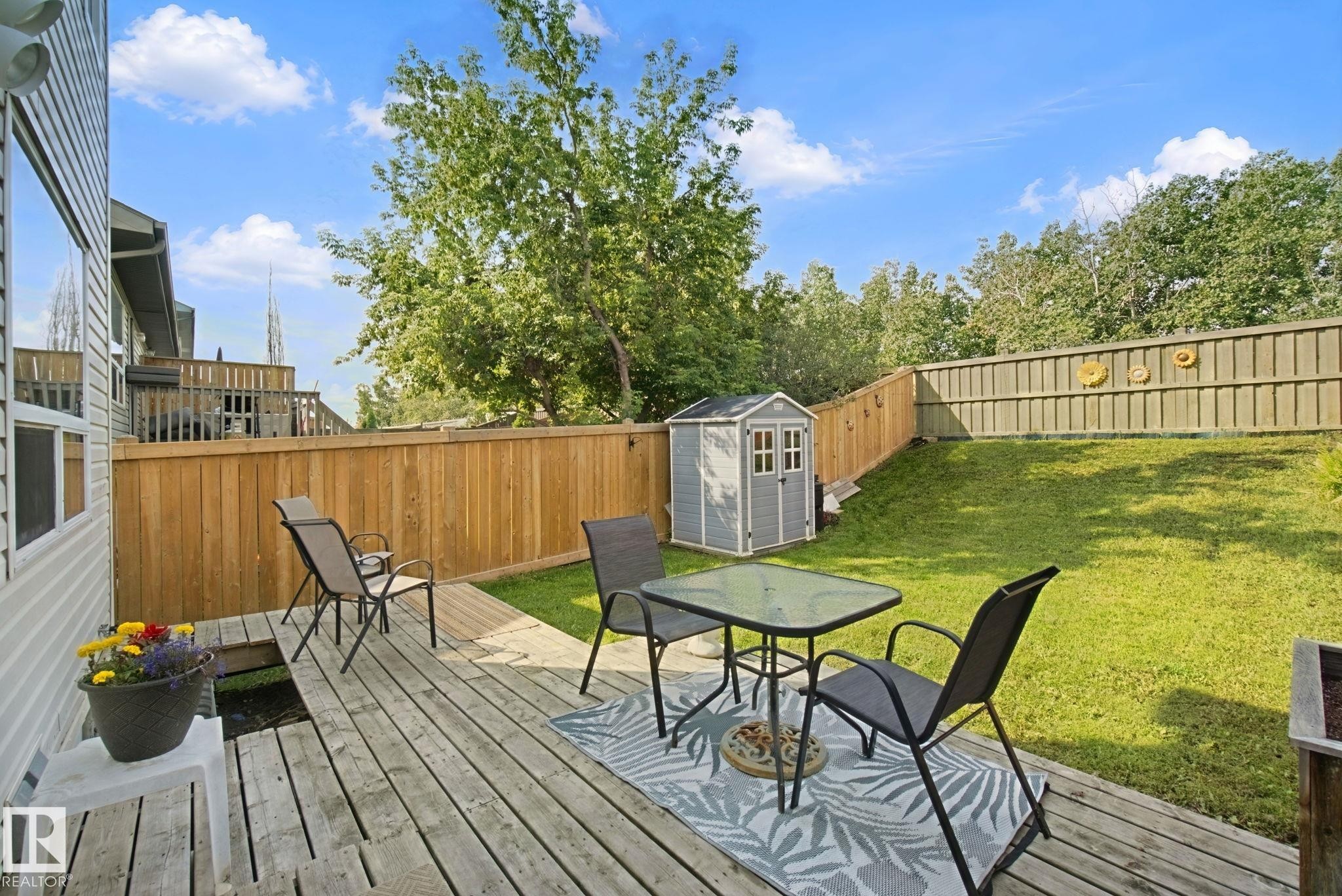 Expansive backyard oasis featuring a composite deck with integrated seating area, mature landscaping with lush lawn, wooden privacy fencing, and a detached storage shed - 15618 141 Street Nw, Edmonton, AB