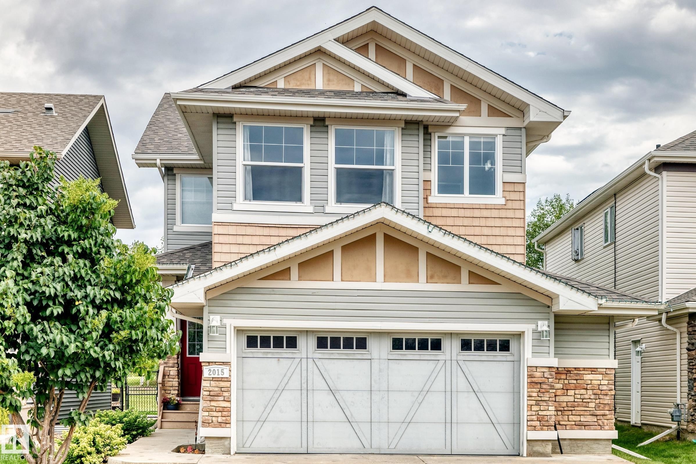 Two-story facade with light gray siding, cedar shake accents, and stone detailing - 2015 Chalmers Way Sw, Edmonton, AB