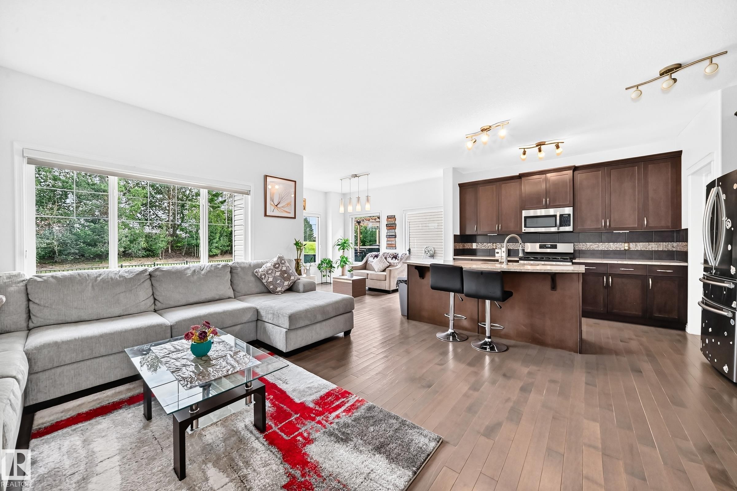 Open concept living area featuring wood-finish flooring, a kitchen island with seating, stainless steel appliances, and large windows - 2015 Chalmers Way Sw, Edmonton, AB