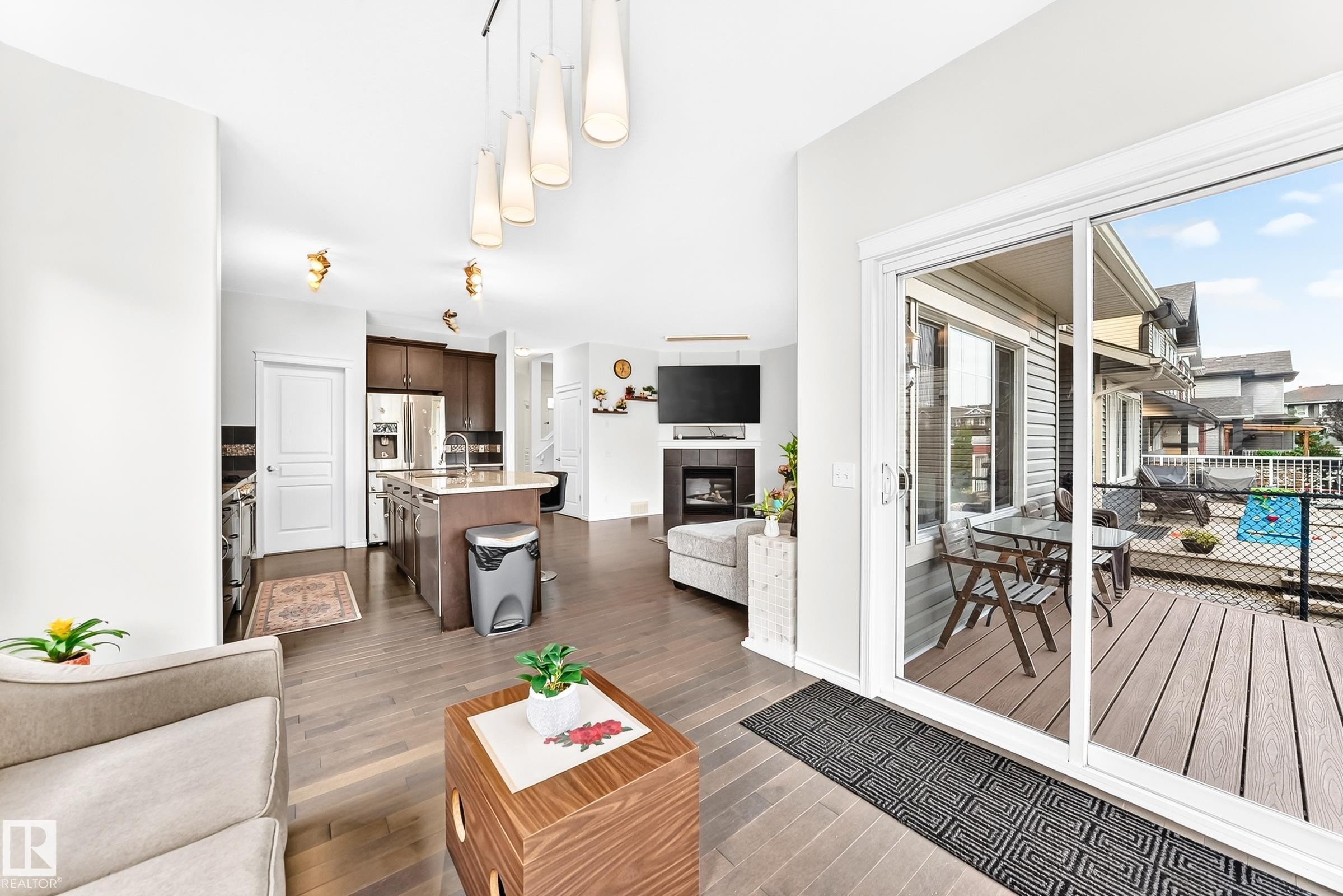 Wood-finish flooring, sliding glass patio door, island kitchen with stainless steel appliances, and a fireplace with a mounted television - 2015 Chalmers Way Sw, Edmonton, AB