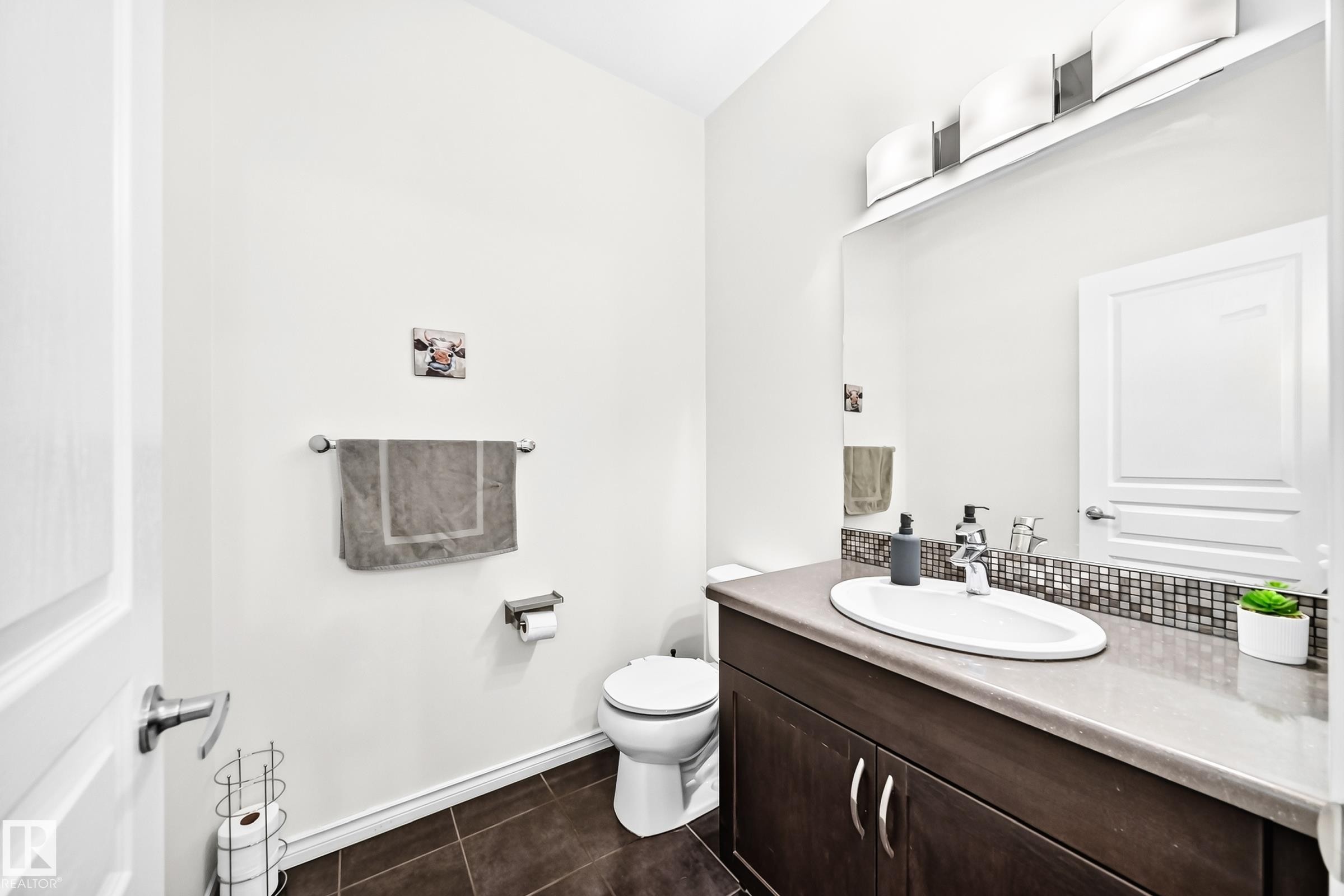 Wood-finish vanity with a surface-mount sink, dark countertop, and mosaic tile backsplash - 2015 Chalmers Way Sw, Edmonton, AB