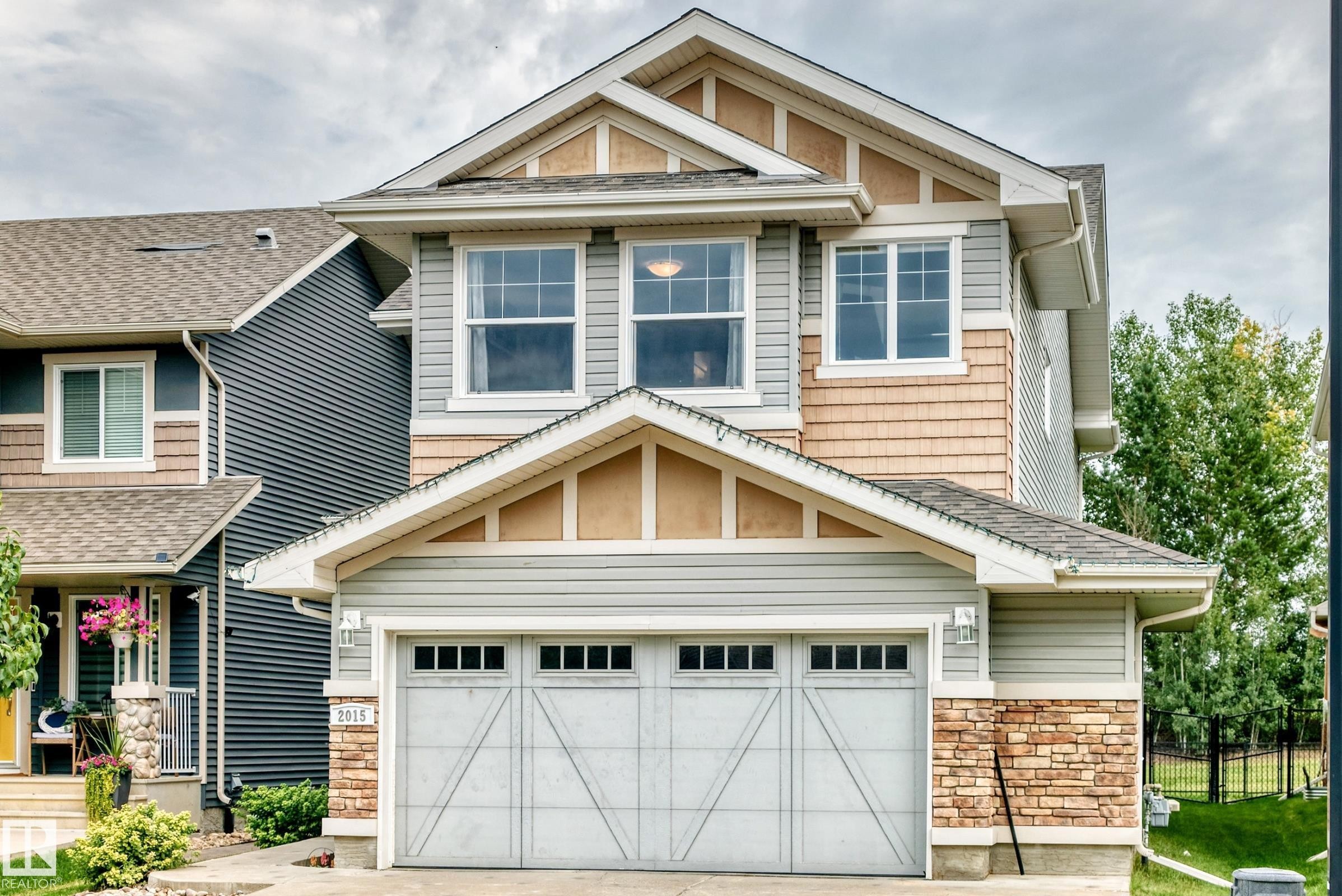 Two-story exterior featuring multi-toned siding, stone accents, and a two-car garage with transom windows - 2015 Chalmers Way Sw, Edmonton, AB