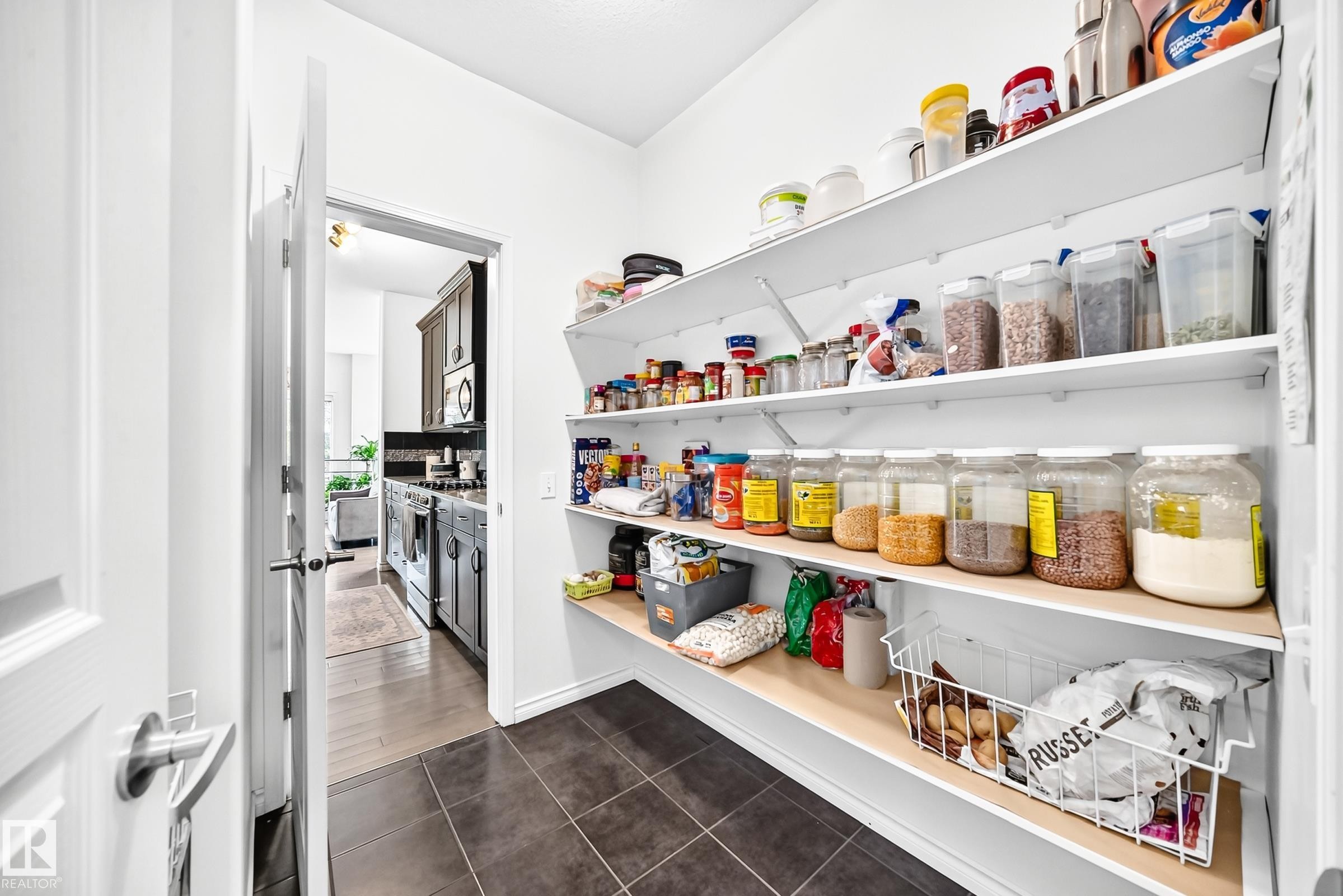 Walk-in pantry with extensive shelving, dark tile flooring, and a white paneled door - 2015 Chalmers Way Sw, Edmonton, AB