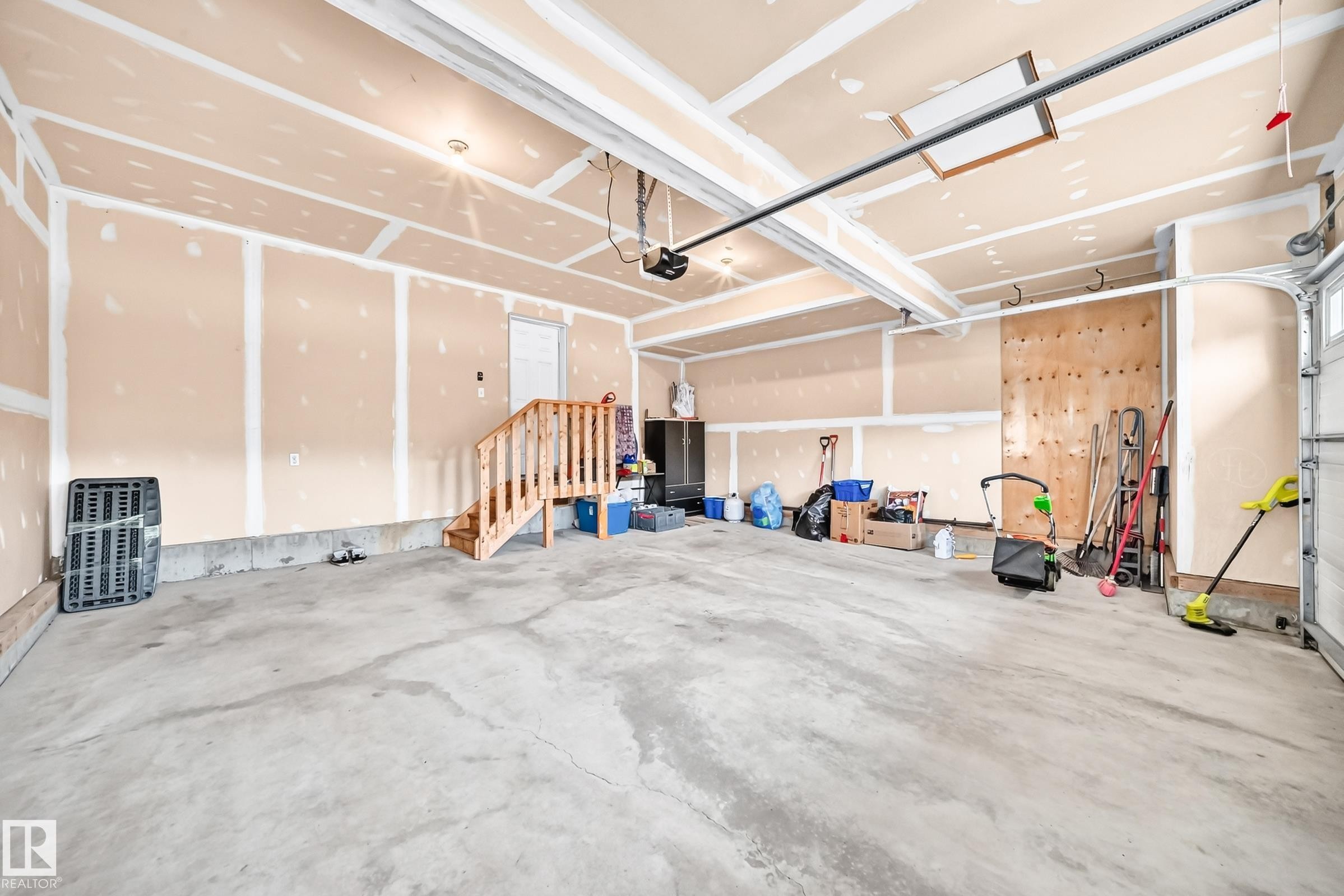 Spacious garage with exposed drywall, concrete flooring, and a built-in wooden staircase - 2015 Chalmers Way Sw, Edmonton, AB