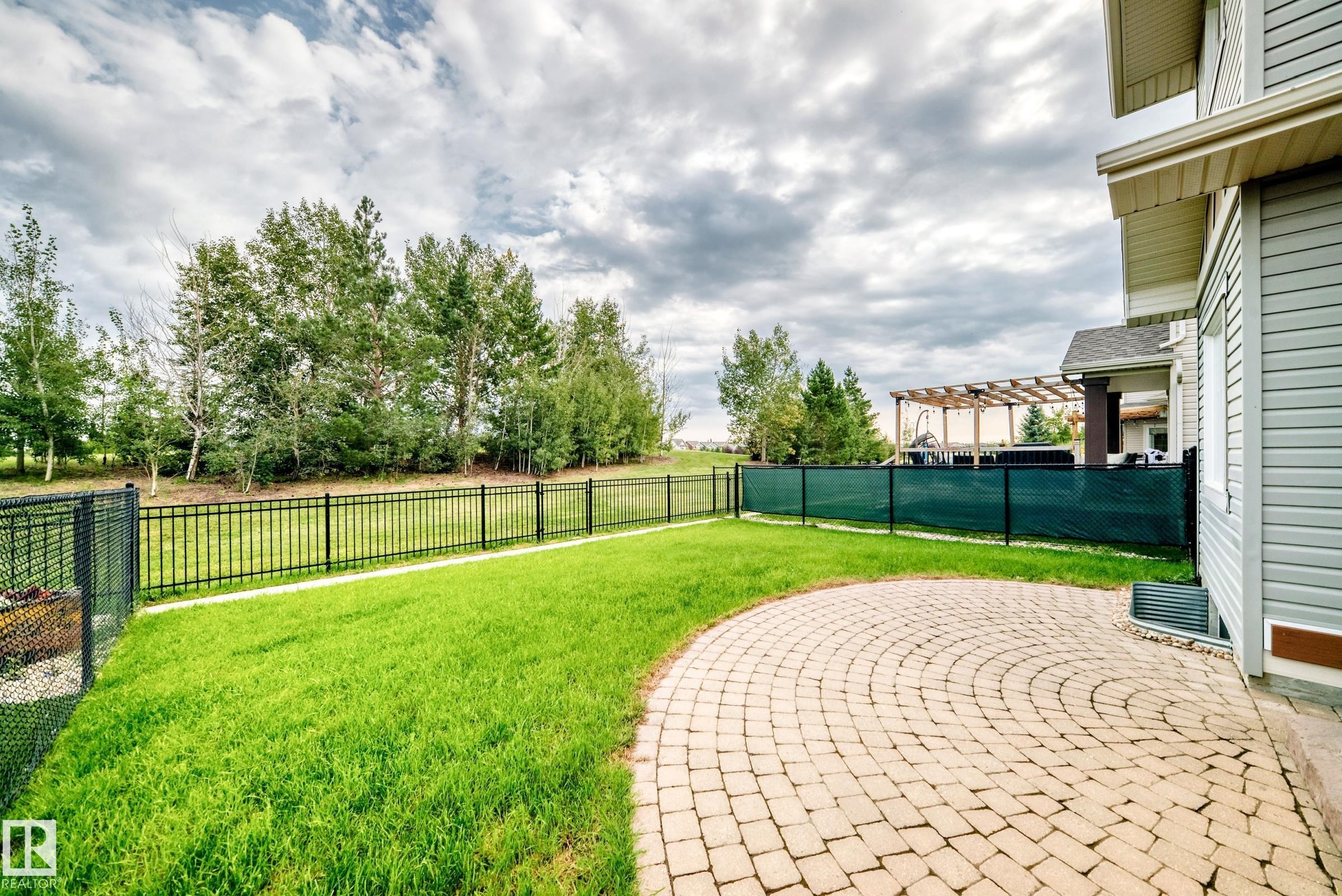 Expansive backyard featuring a manicured lawn, a curved paver patio, and a black wrought-iron fence - 2015 Chalmers Way Sw, Edmonton, AB