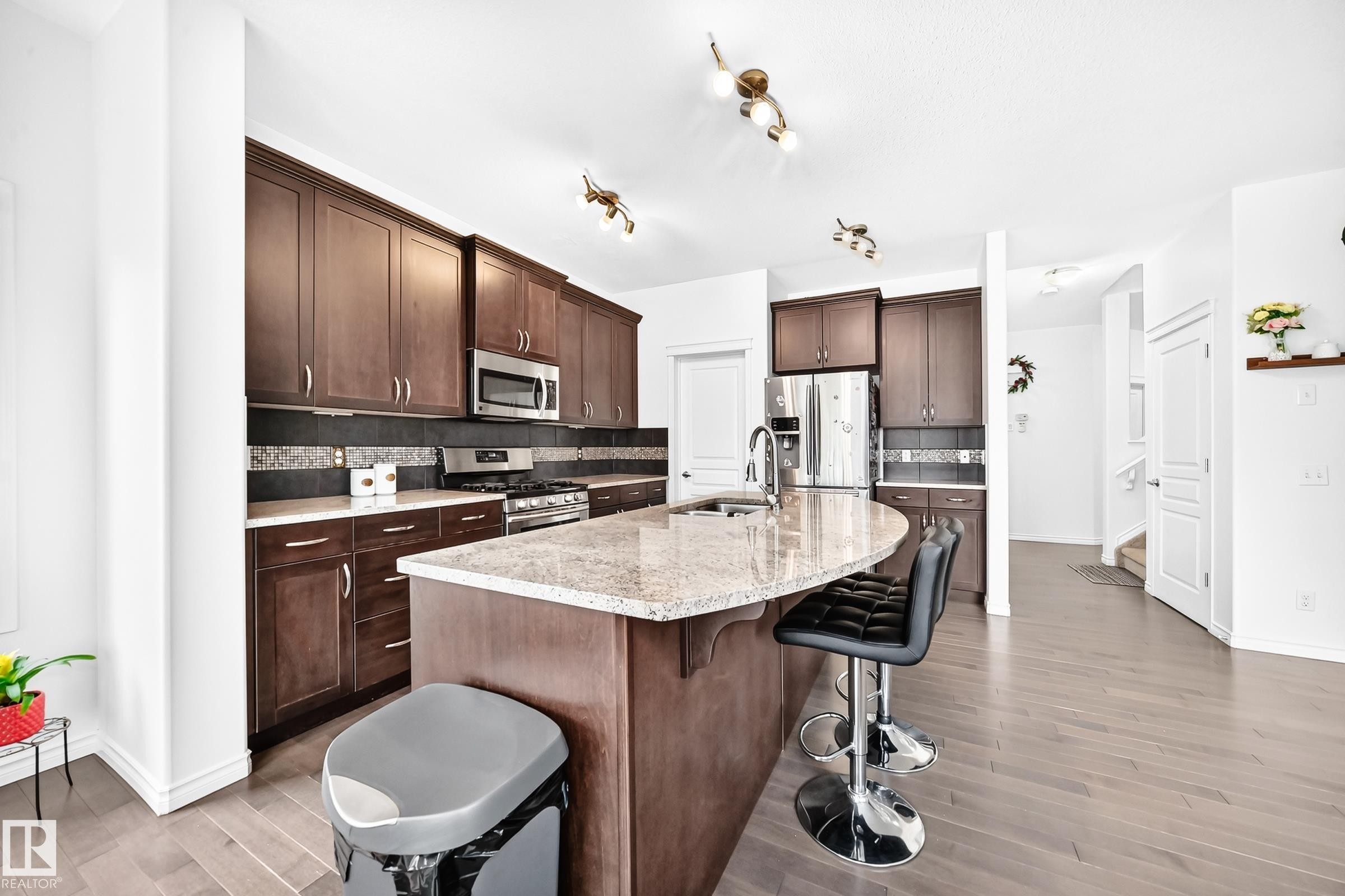 Spacious kitchen featuring dark wood cabinetry, stainless steel appliances, a large center island with a granite countertop, and light wood-finish flooring - 2015 Chalmers Way Sw, Edmonton, AB