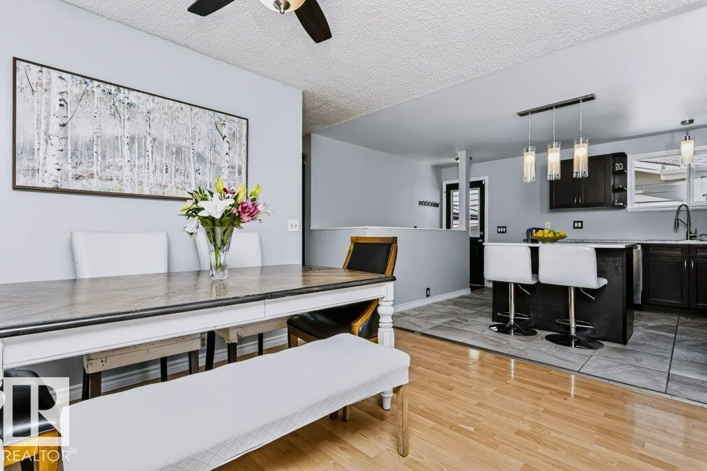 Wood-finish flooring, ceiling fan, kitchen island with breakfast bar, dark wood-finish cabinetry, and pendant lighting - 18431 95A Avenue Nw, Edmonton, AB