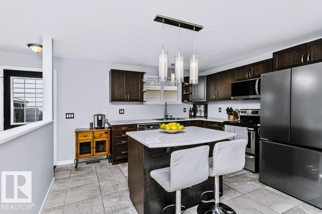 Kitchen featuring a central island with countertop, dark wood-finish cabinetry, stainless steel appliances, and tiled flooring - 18431 95A Avenue Nw, Edmonton, AB