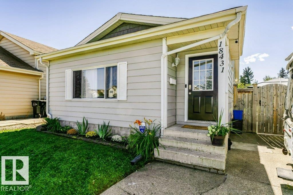 Light gray horizontal siding with white trim, a black front door with glass panels, and a concrete pathway - 18431 95A Avenue Nw, Edmonton, AB