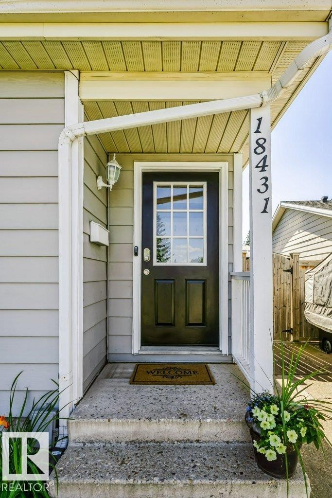 Covered front entryway with concrete steps, black paneled door with glass inserts, wall-mounted exterior light fixture, and vertical house numbers - 18431 95A Avenue Nw, Edmonton, AB