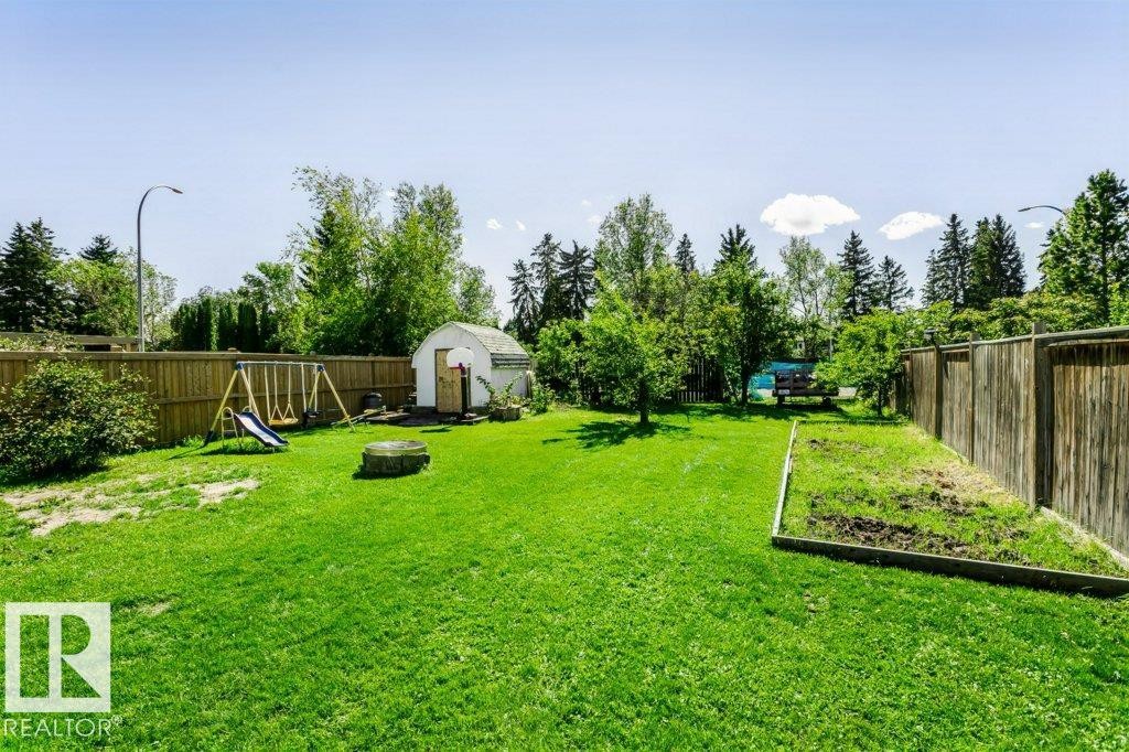 Expansive fenced yard featuring a storage shed, mature trees, and a dedicated garden plot - 18431 95A Avenue Nw, Edmonton, AB
