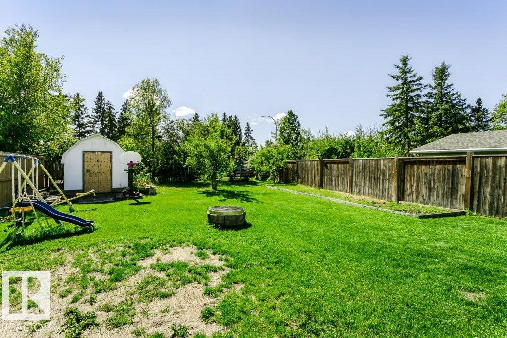 Expansive grassy yard featuring mature trees, a storage shed with double doors, and wood fencing - 18431 95A Avenue Nw, Edmonton, AB