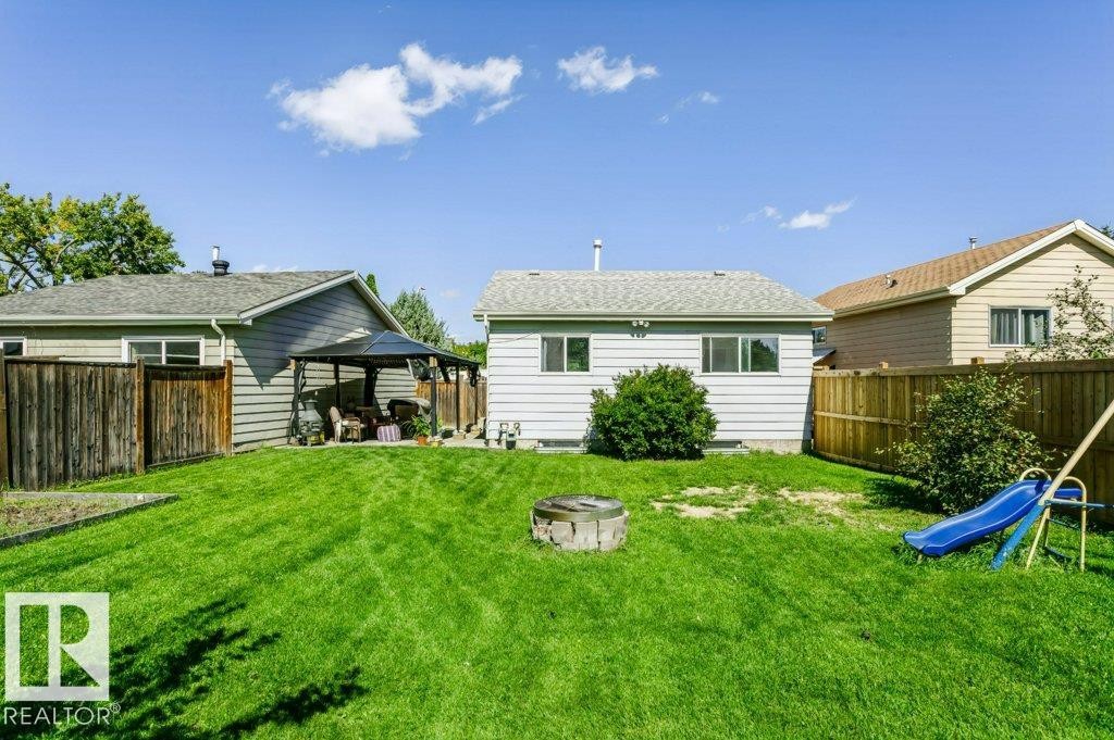 Expansive grassy yard featuring a fenced perimeter, a covered patio area, and a fire pit - 18431 95A Avenue Nw, Edmonton, AB
