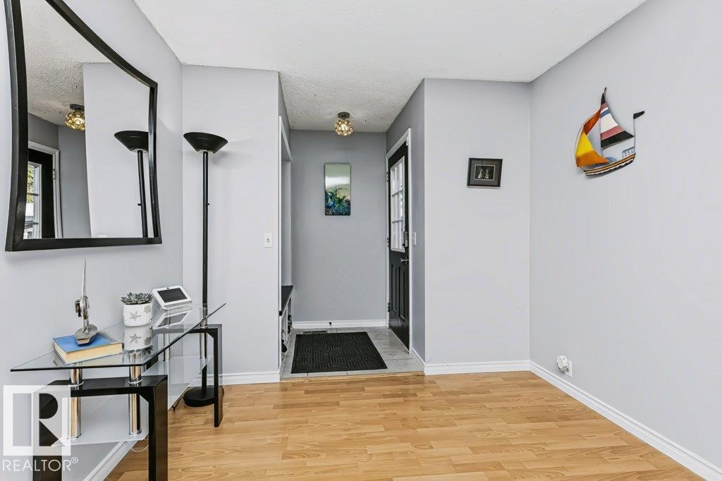 Light wood-finish flooring with white trim, light gray wall paint, and a front entry door with glass paneling - 18431 95A Avenue Nw, Edmonton, AB