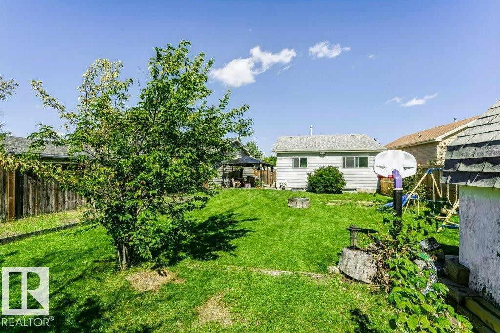 Expansive grassy yard featuring a mature tree, privacy fencing, and a detached structure with siding - 18431 95A Avenue Nw, Edmonton, AB
