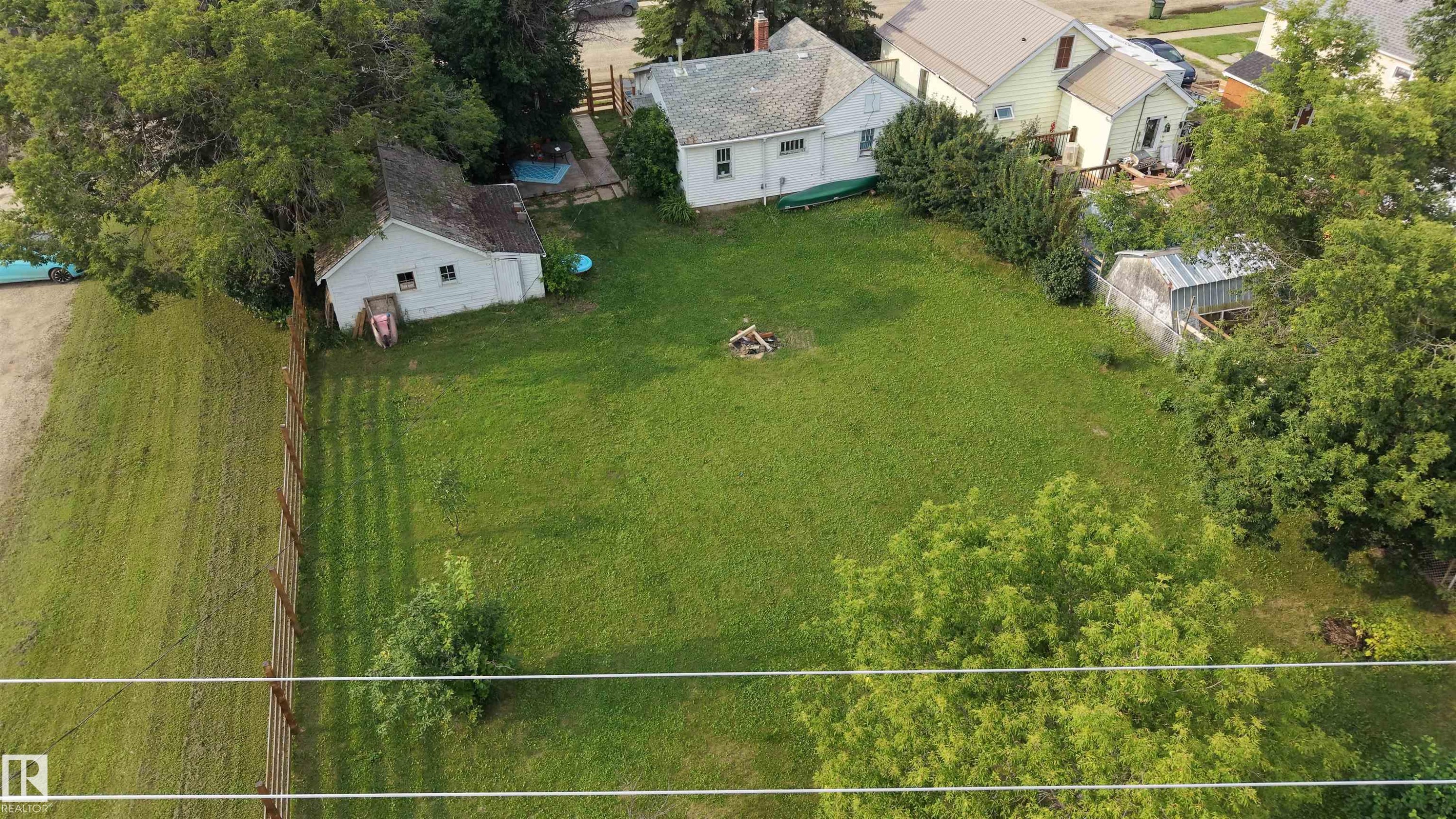 Expansive green lawn with mature trees and perimeter fencing. showing the home and garage - 5019 48 Avenue, Onoway, AB - Outdoor