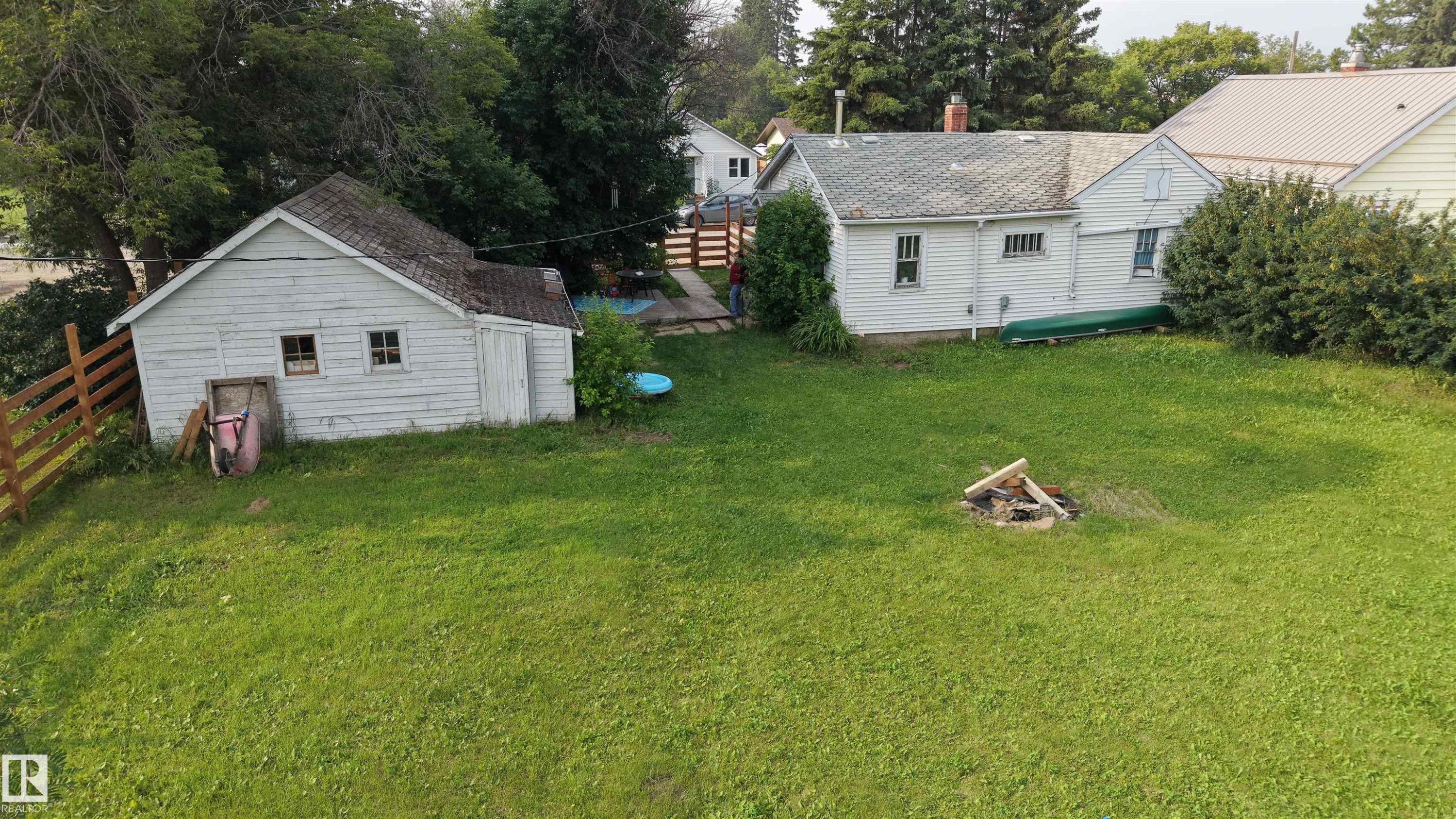 Expansive green space featuring a white wood-sided shed with a shingle roof and two windows, and a home to match - 5019 48 Avenue, Onoway, AB - Outdoor