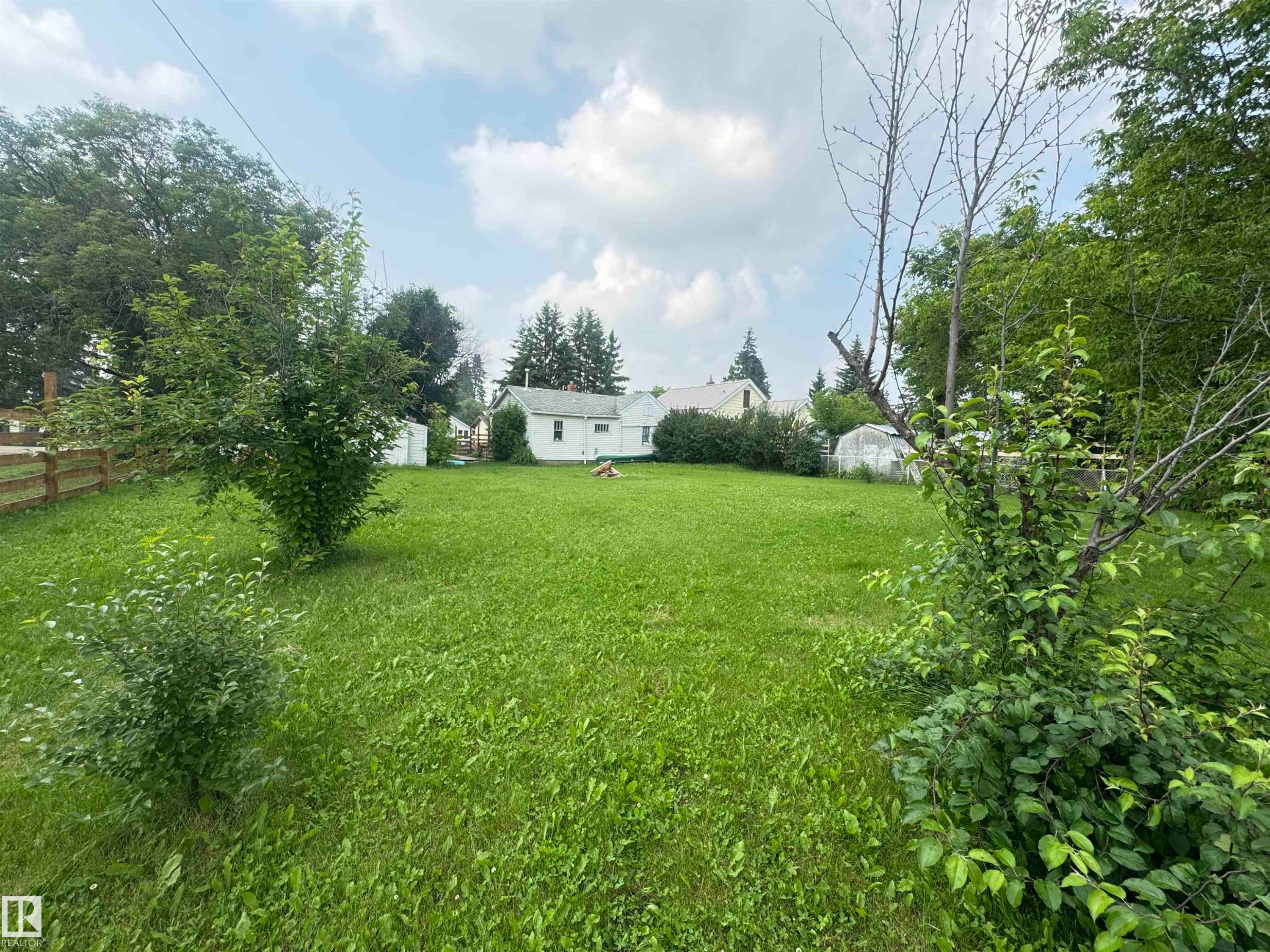 Expansive green lawn with mature trees and a partial wood fence - 5019 48 Avenue, Onoway, AB - Outdoor